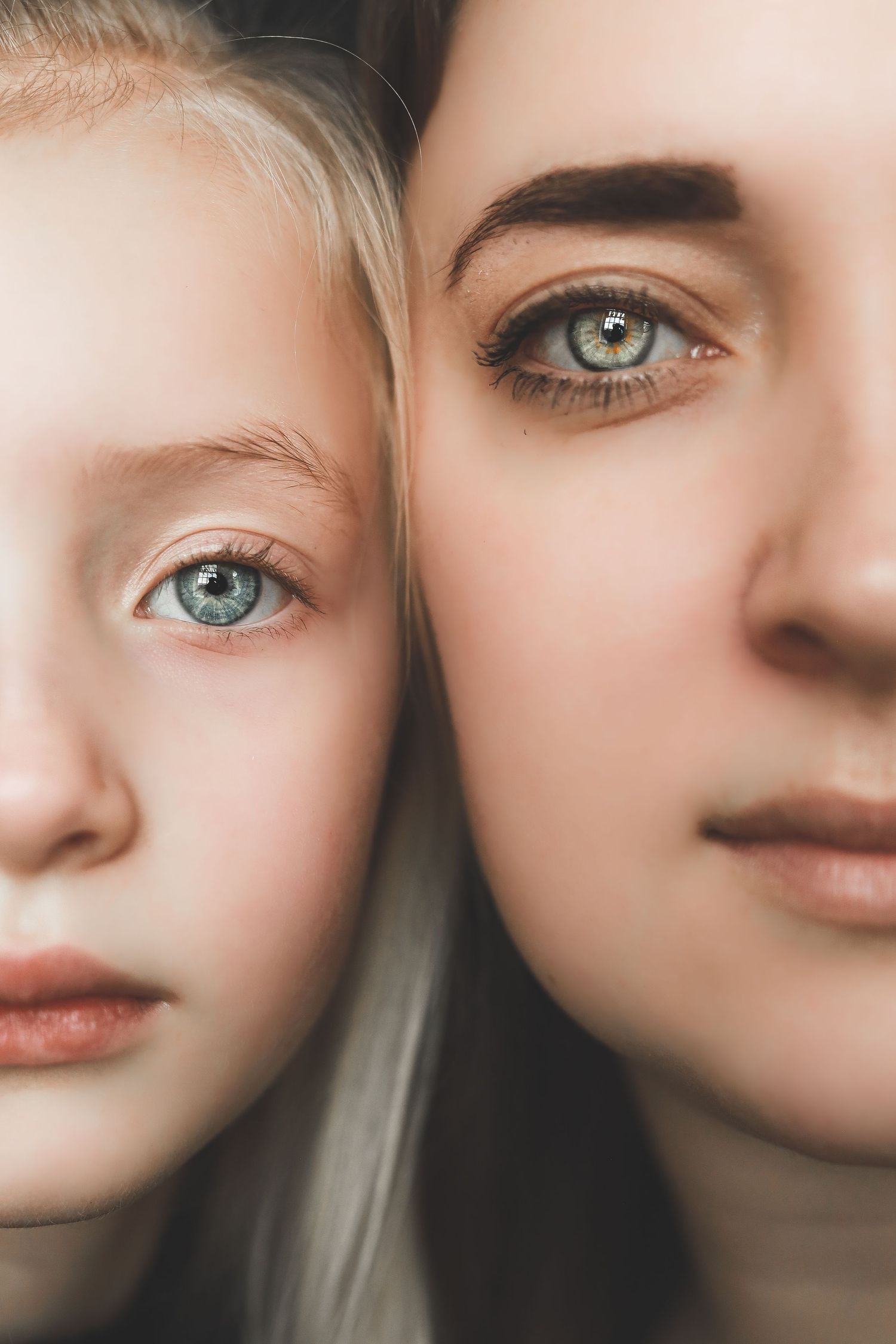 Close-up portrait of a blonde girl and young woman with matching blue-green eyes leaning their faces together.