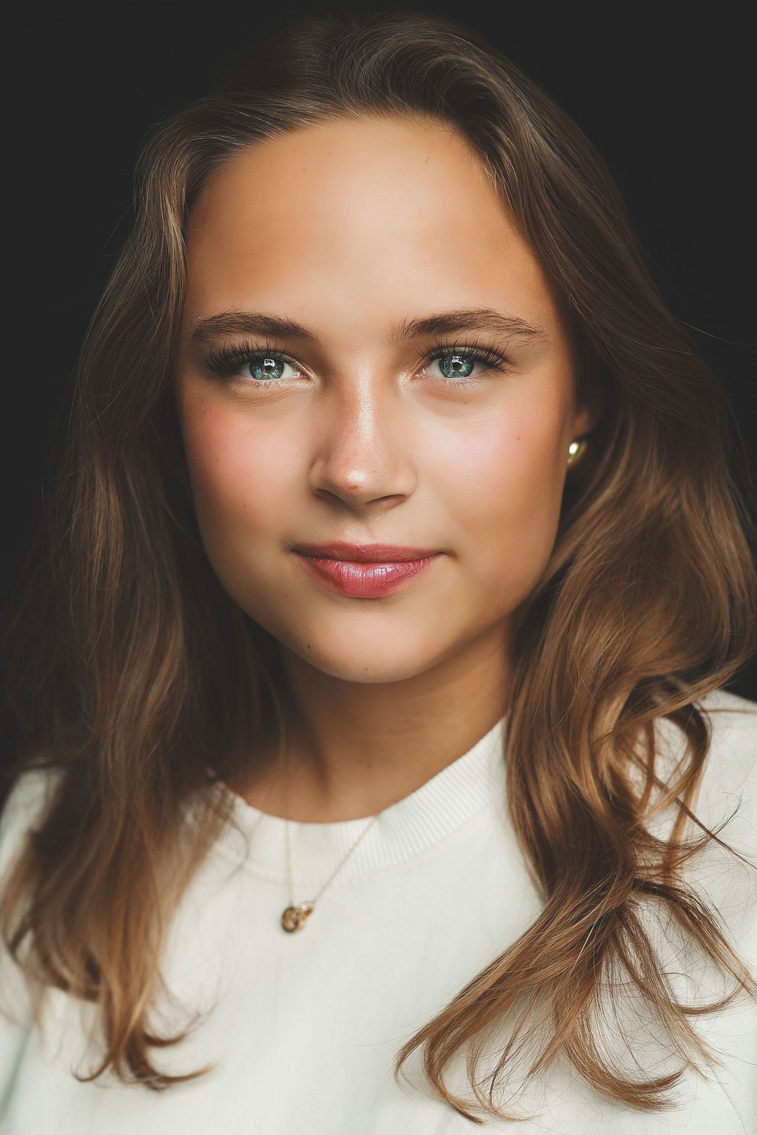 Portrait of a teenage girl with long brown hair and blue-green eyes wearing a white top.