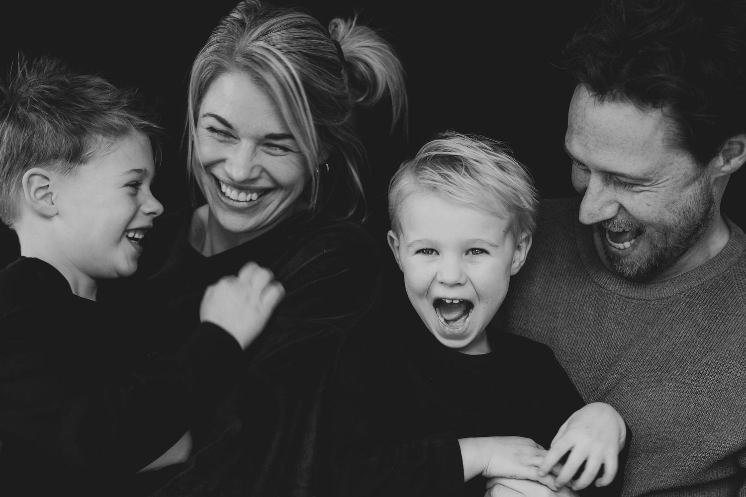 Black and white portrait of laughing family of four sharing a joyful candid moment.