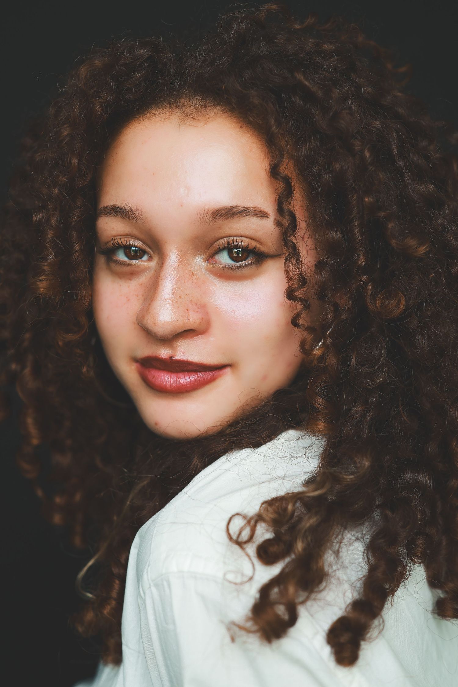 Portrait of a young woman with curly auburn hair freckles and green eyes in a white shirt.