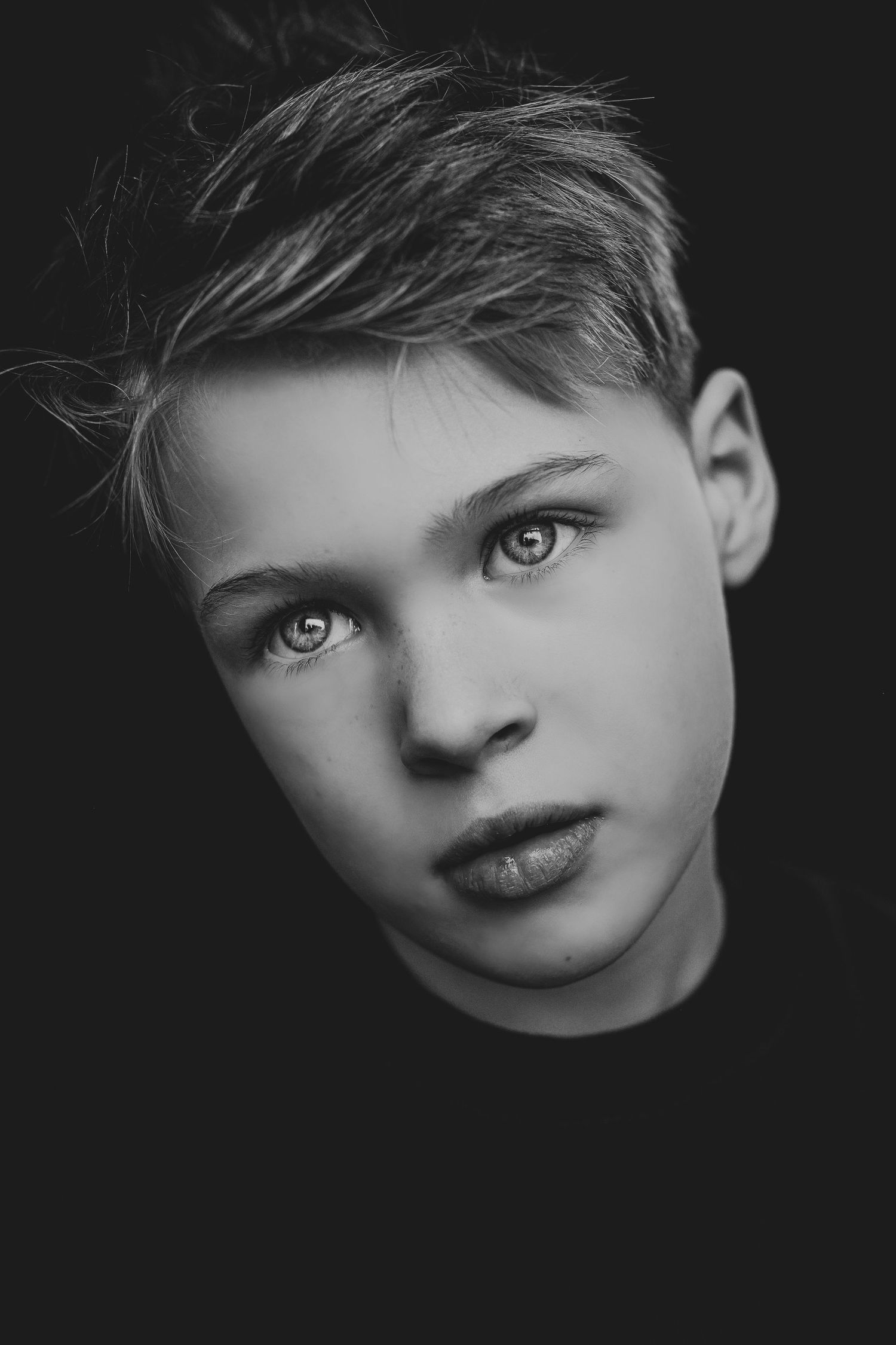 Striking black and white close-up portrait of a young boy with expressive eyes and stylish hair.