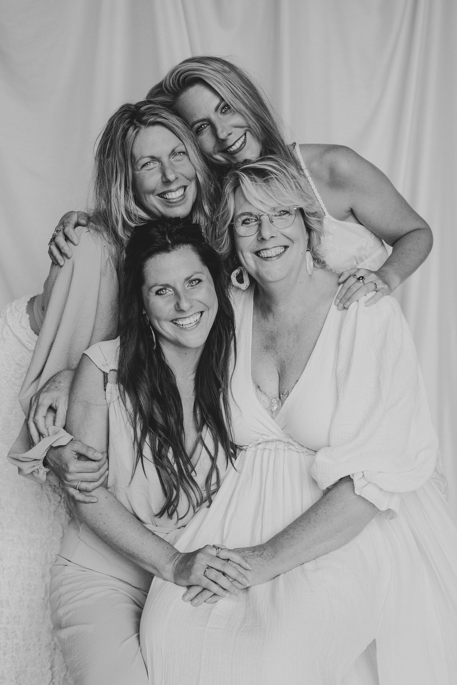 Black and white studio portrait of four smiling women of different ages posing closely together.