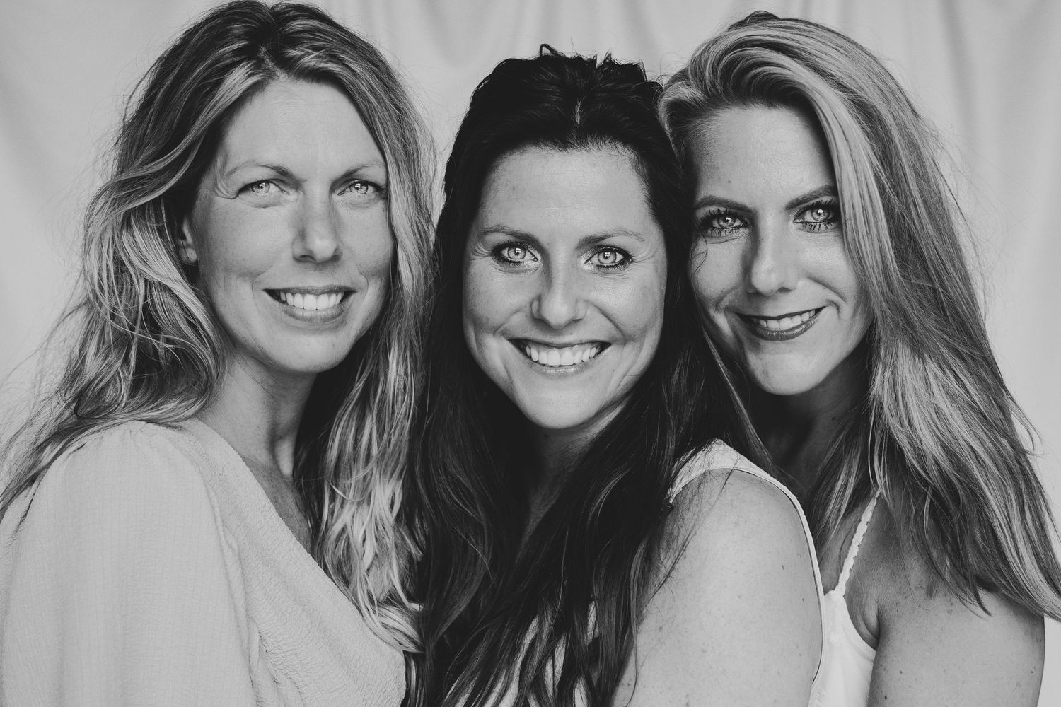 Black and white close-up portrait of three smiling women posing together outdoors.
