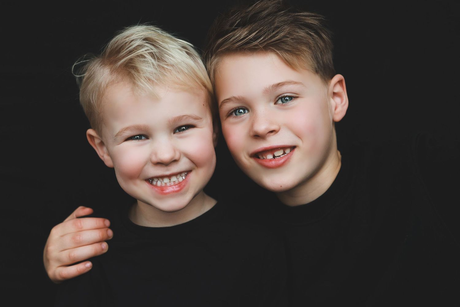 Black and white photo of two young brothers in black shirts smiling and posing together closely.