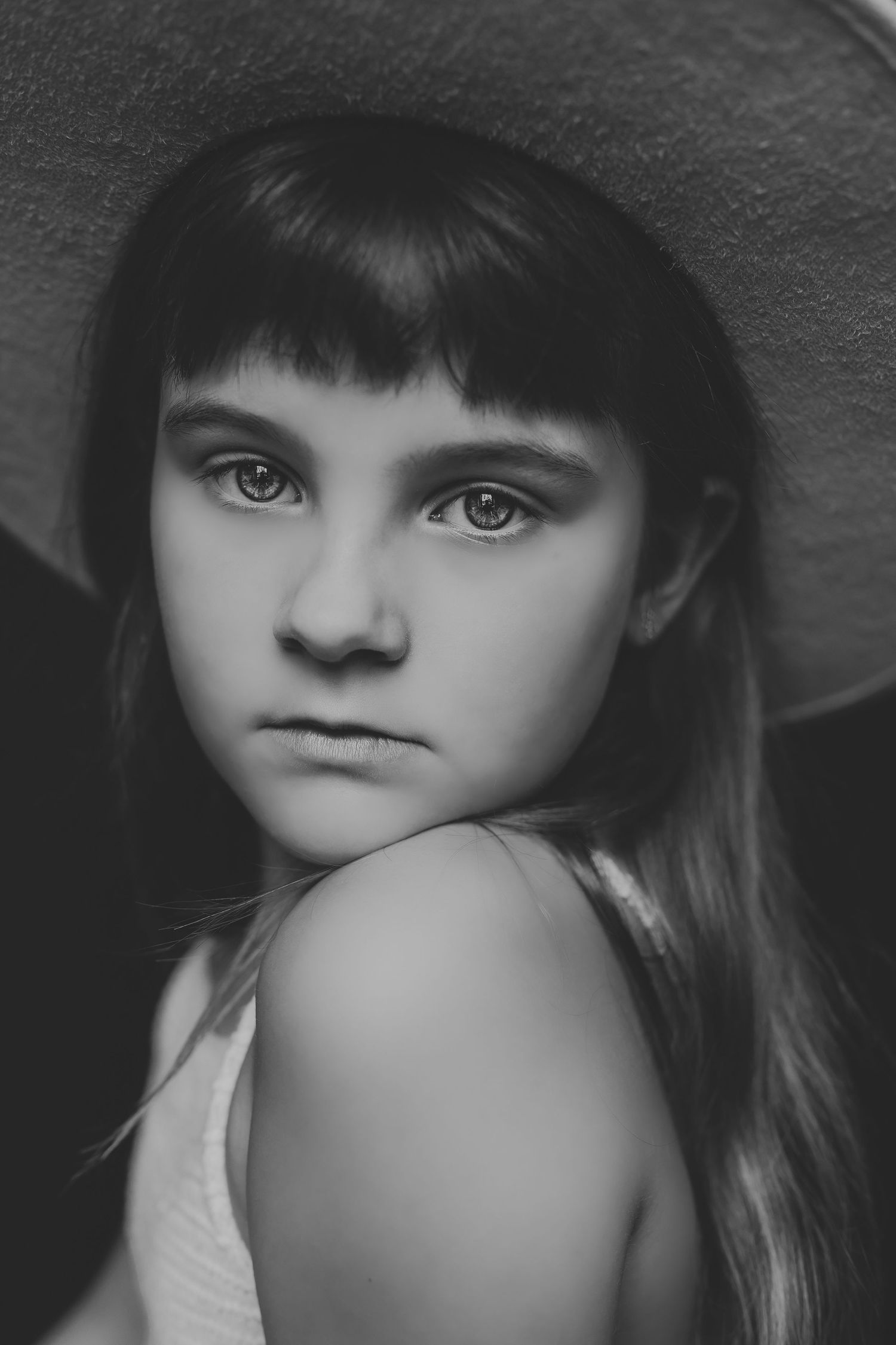 Black and white portrait of a young girl with bangs wearing a wide-brim hat, looking at the camera.