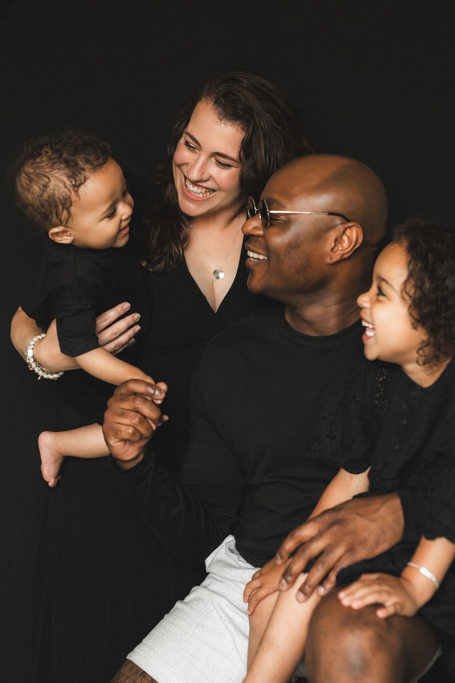 Happy interracial family of four laughing together in matching black outfits studio portrait.