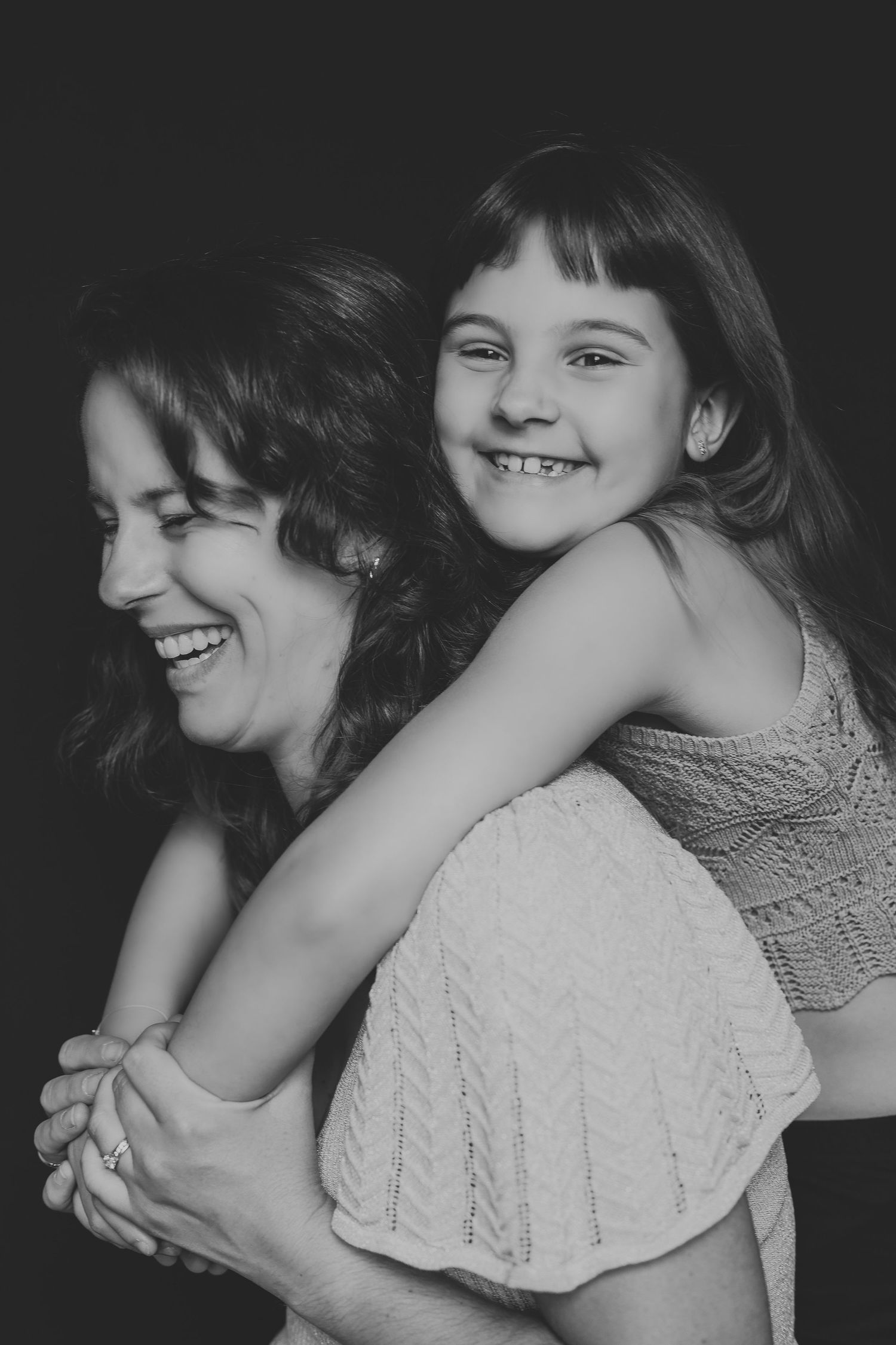Black and white photo of a smiling mother and daughter sharing a joyful piggyback moment together.