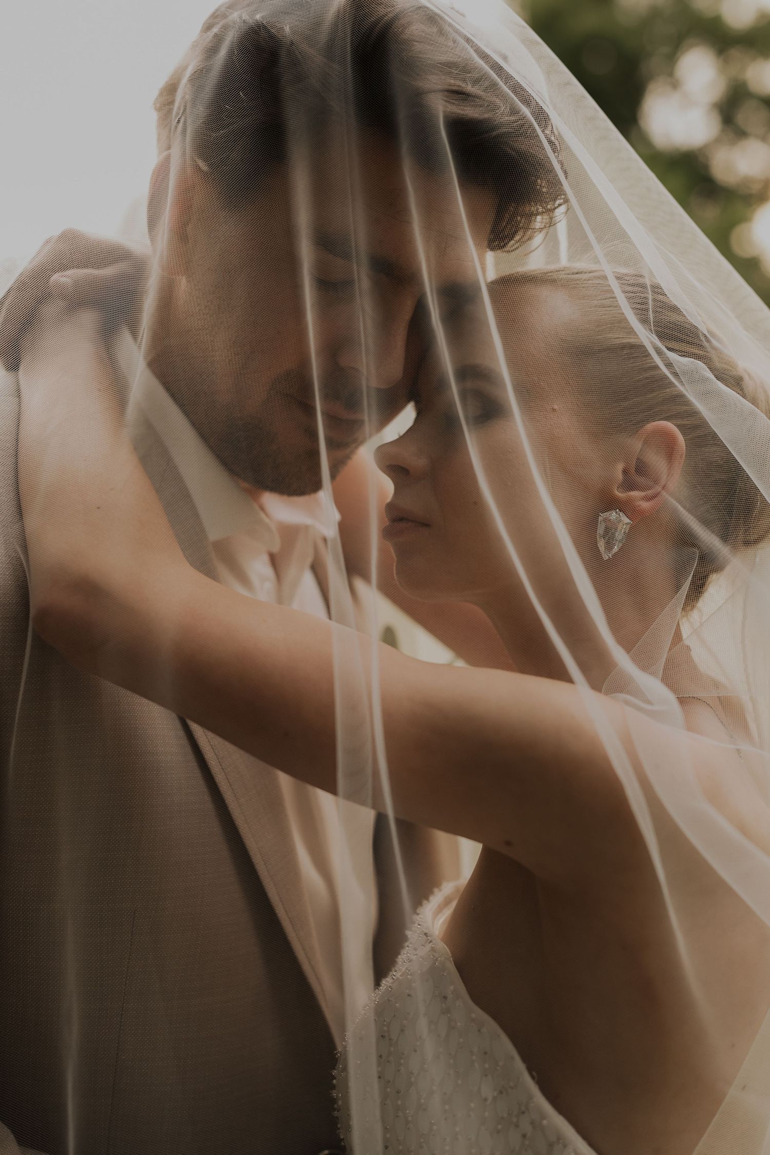 Bride and groom sharing an intimate moment under a flowing wedding veil outdoors.