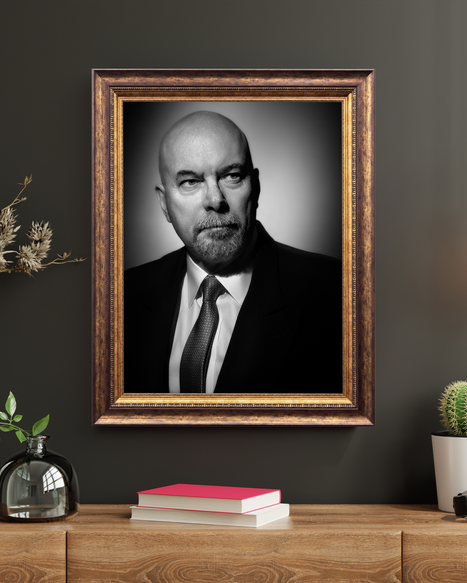 Black and white framed portrait of a bald bearded man in a suit displayed on a dark wall above a wooden shelf.