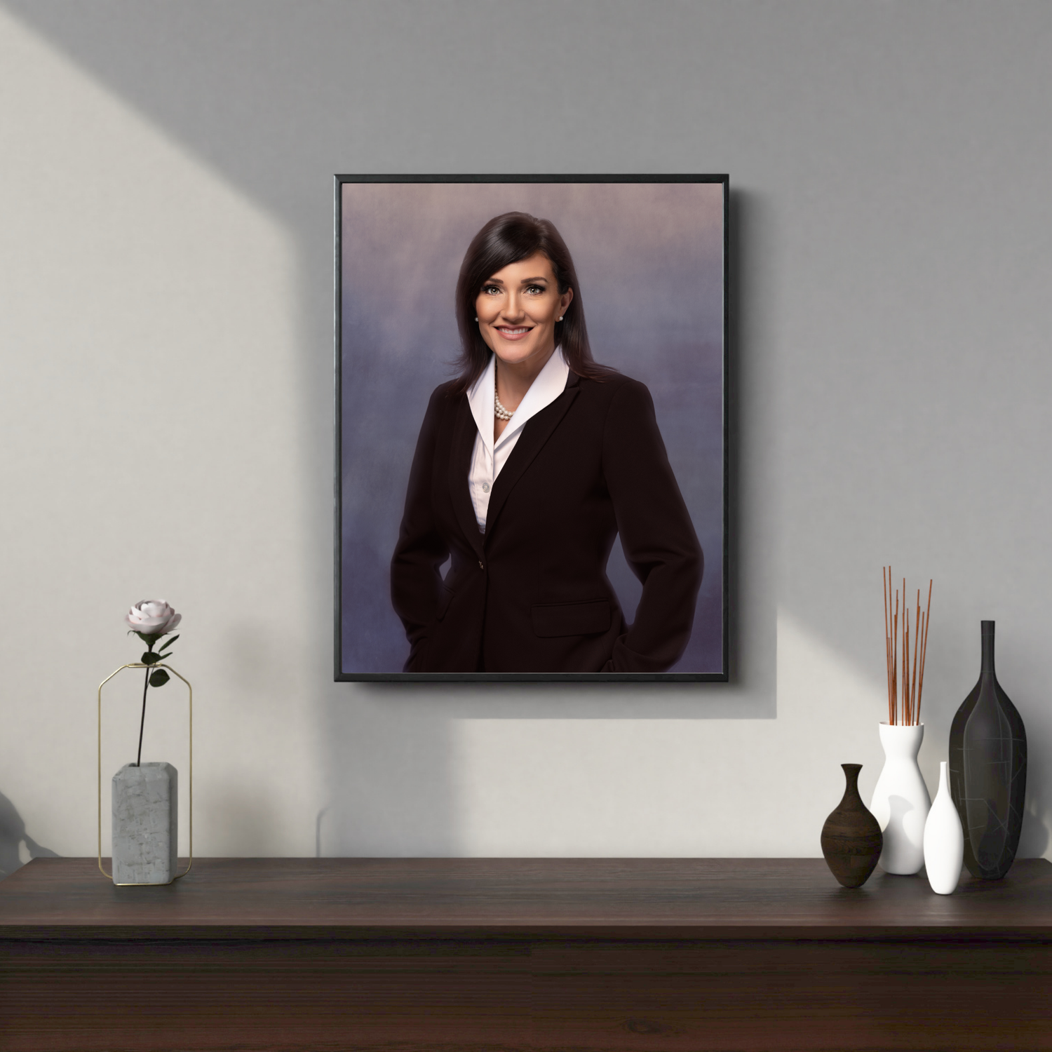 Framed portrait of a smiling woman in a dark blazer displayed on a wall above a wooden console with decorative vases.