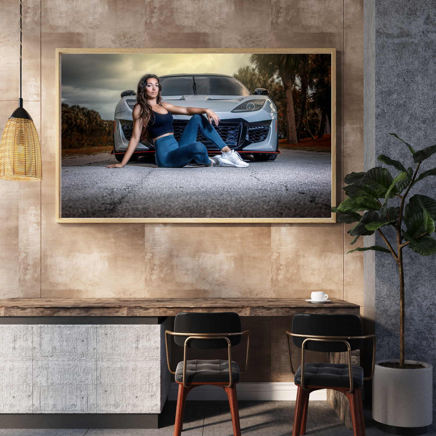 A woman in jeans sits in front of a silver sports car, displayed as framed wall art in a modern industrial dining space.