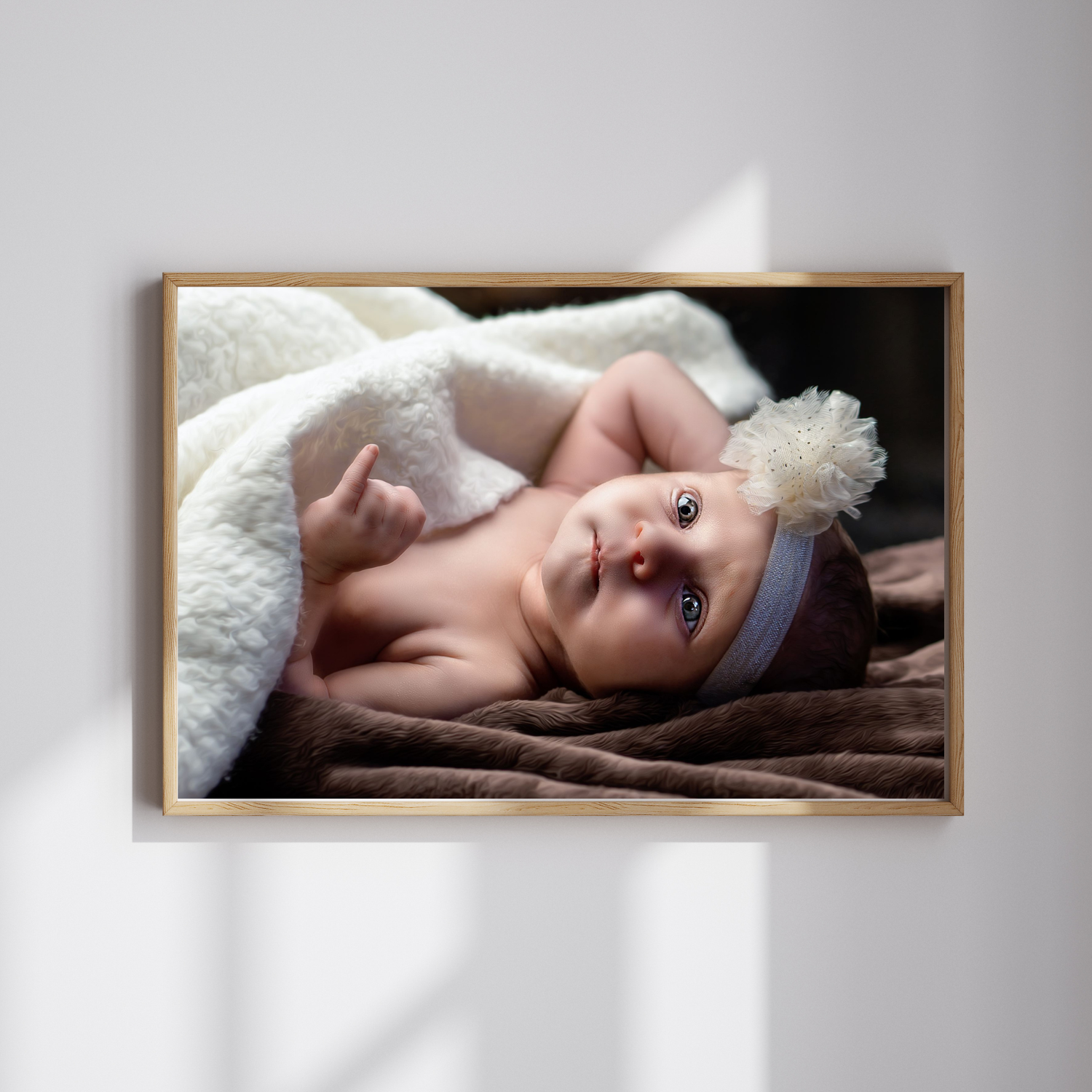 Newborn baby with blue eyes wearing a floral headband, wrapped in a white fluffy blanket on a brown surface.