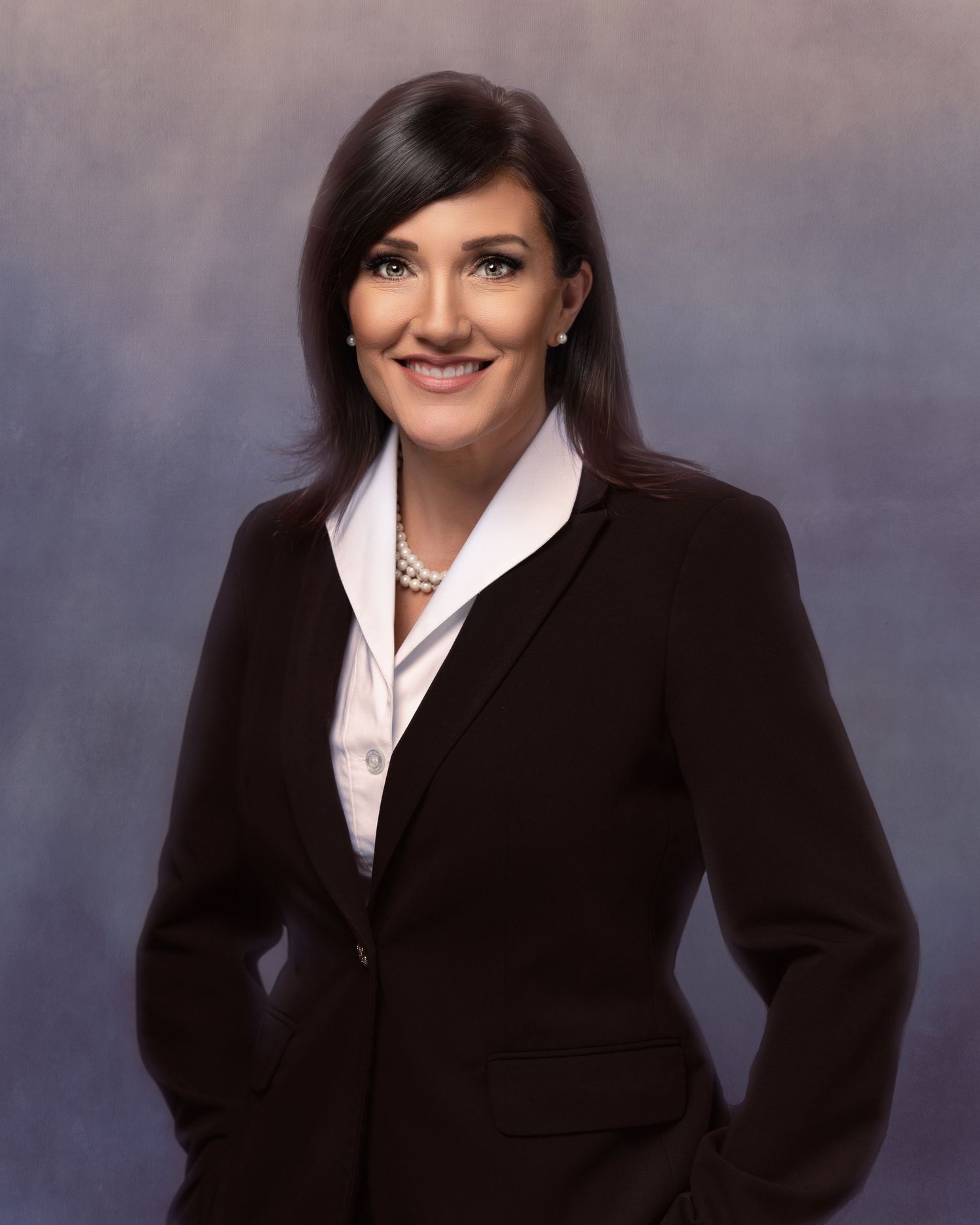Professional woman in dark blazer and pearl necklace poses confidently for a formal business portrait photo.