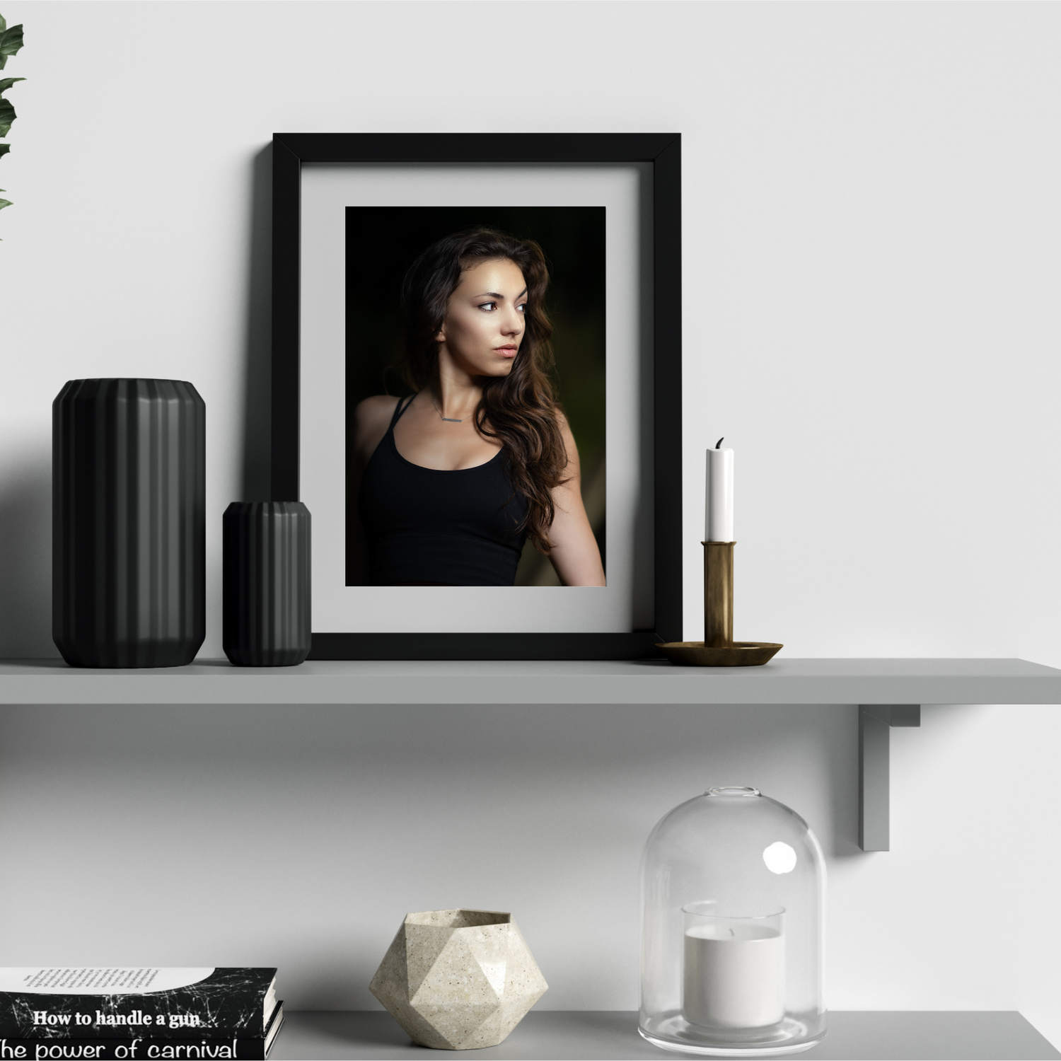 Framed portrait of a woman in a black top displayed on a shelf with decorative vases, candle, and geometric objects.