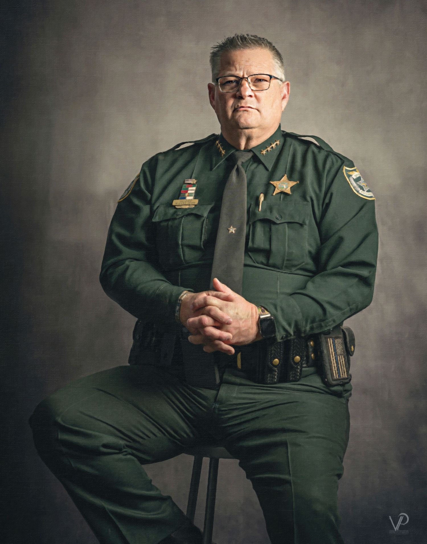 A sheriff in a green uniform with a gold star badge sits confidently with hands clasped in a professional portrait.