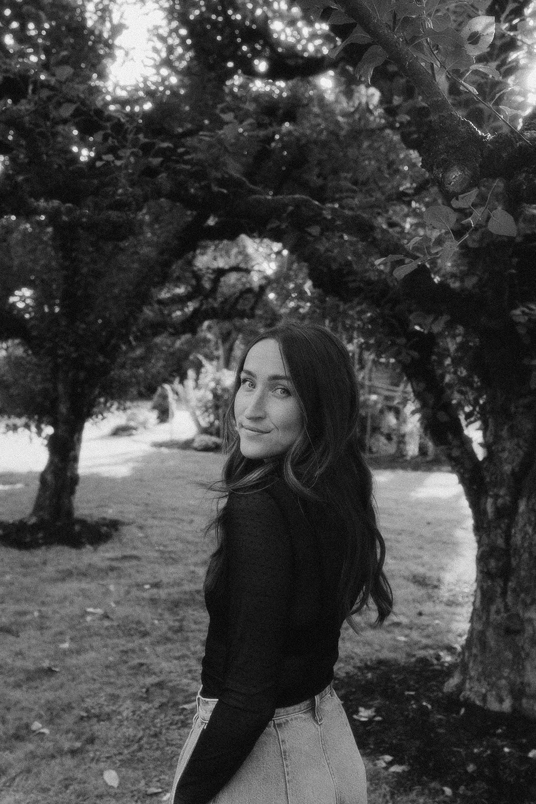 a black and white image of Erin Johnston taken under apple tress