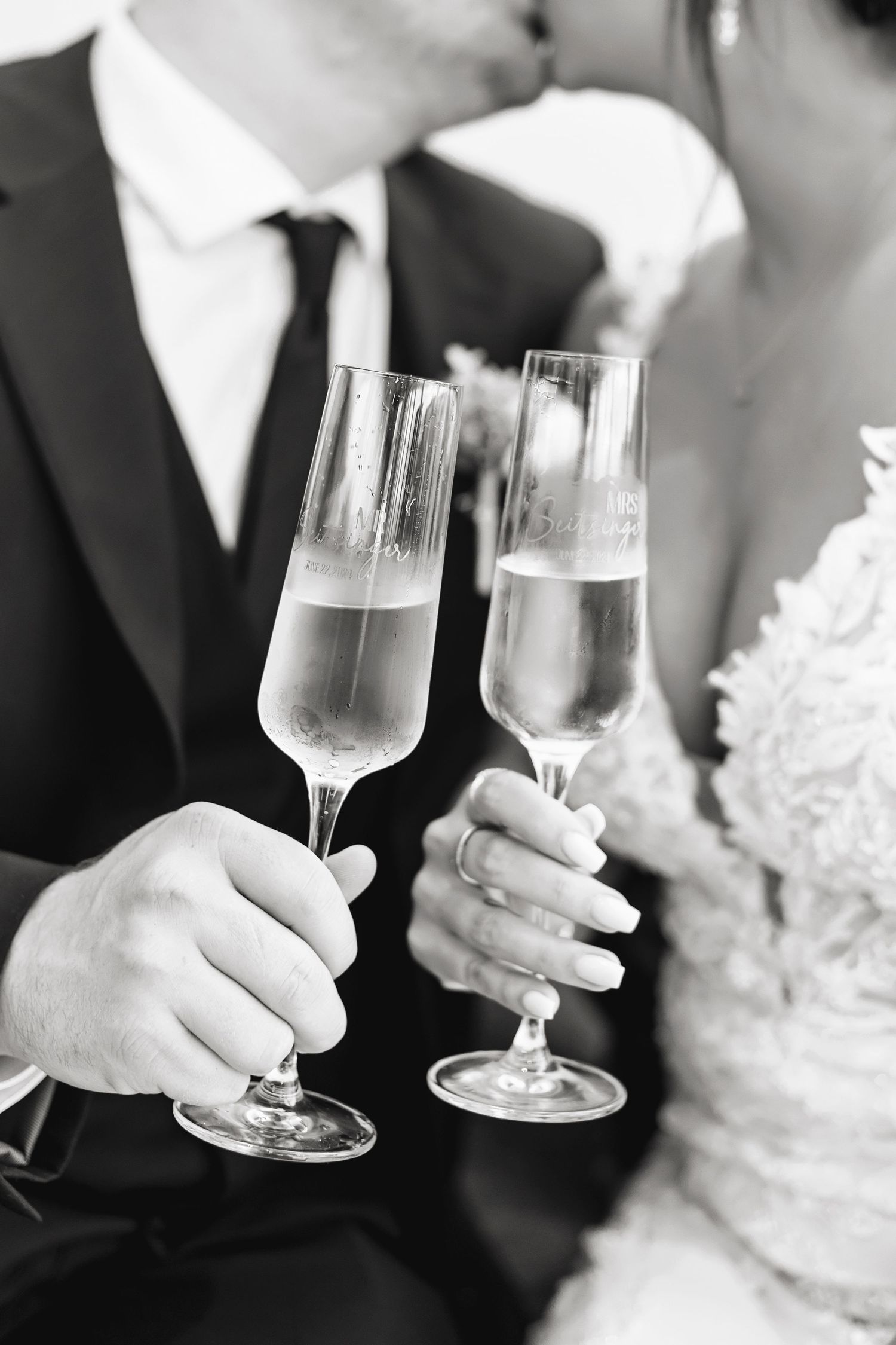 Black and white photo of bride and groom kissing while holding champagne flutes at wedding reception.