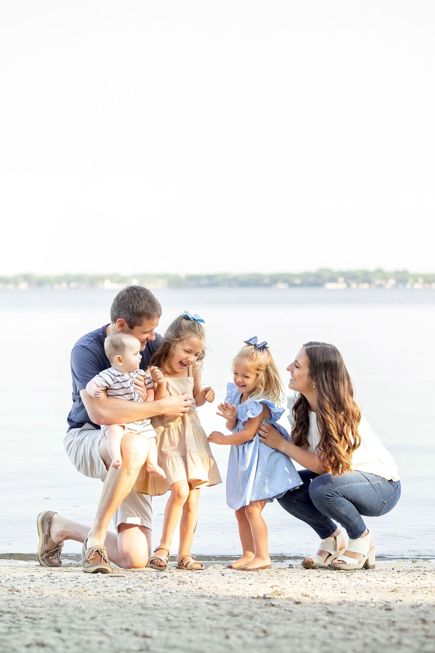 Happy family with three young children enjoying a family photography session on the beach by the water in Clear Lake, Iowa.