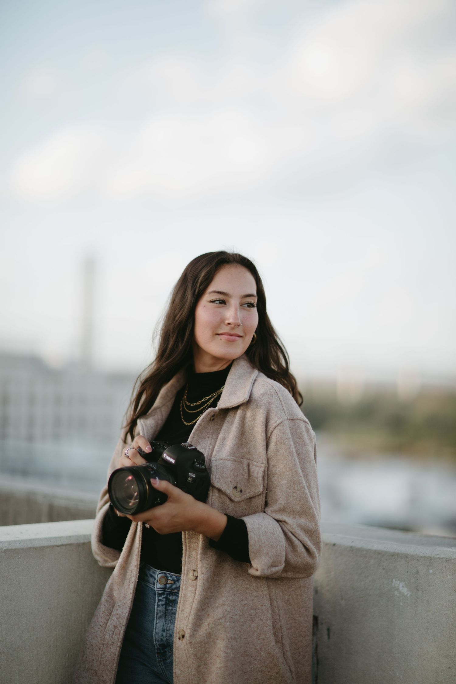 Casual outdoor portrait session featuring tan jacket and denim against urban backdrop.