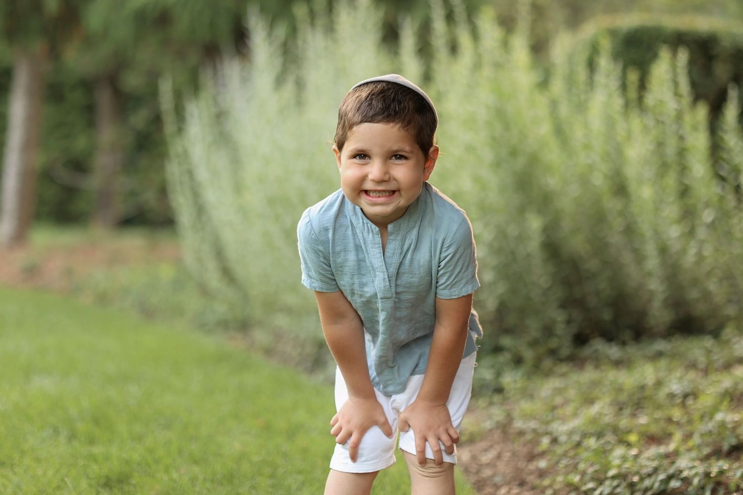 Smiling young boy leaning on his knees in a lush field surrounded by natural beauty