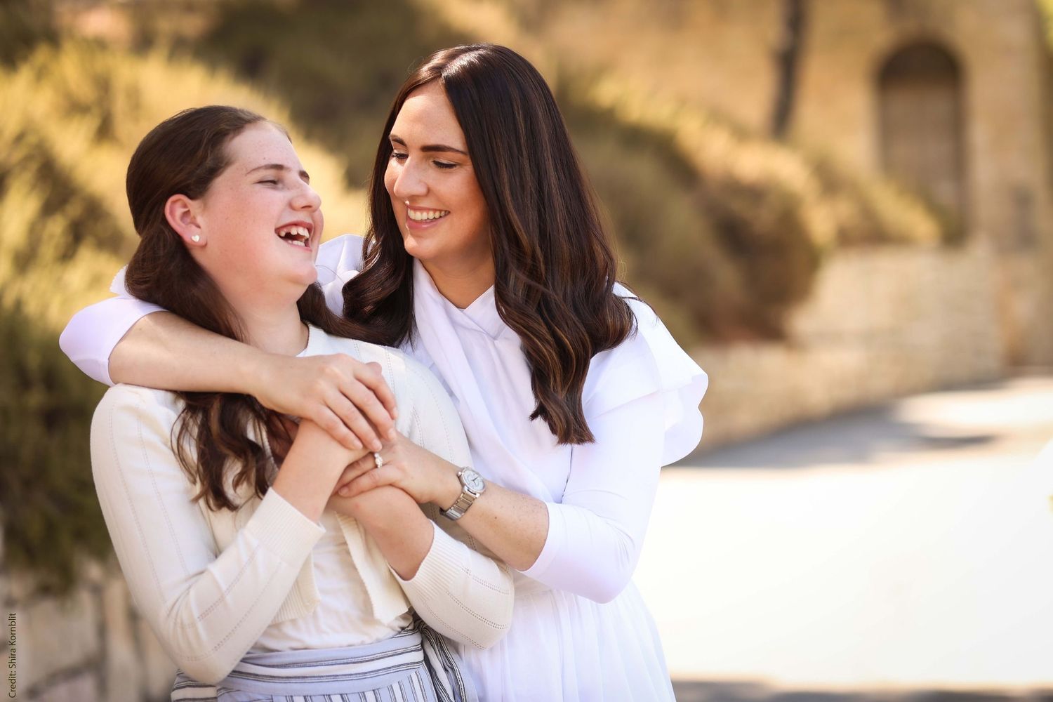 Portrait photographer Gitty sharing a candid, laughing moment with a young girl in a sun-drenched outdoor setting.