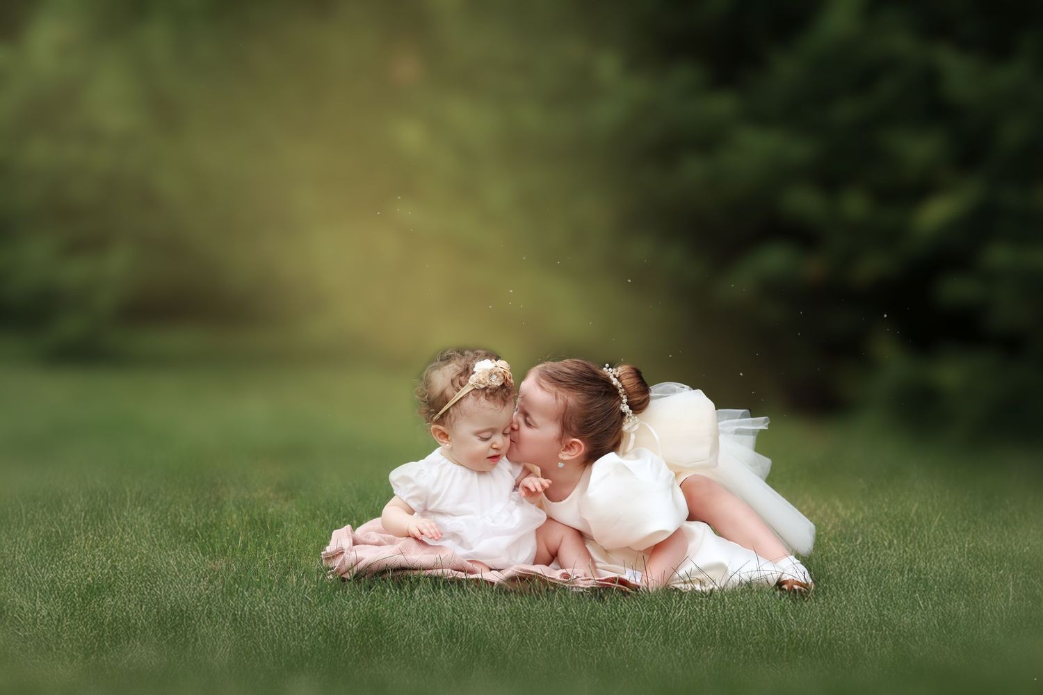 Two young sisters in white dresses share a sweet moment surrounded by soft, dewy grass in a garden in Lakewood, NJ