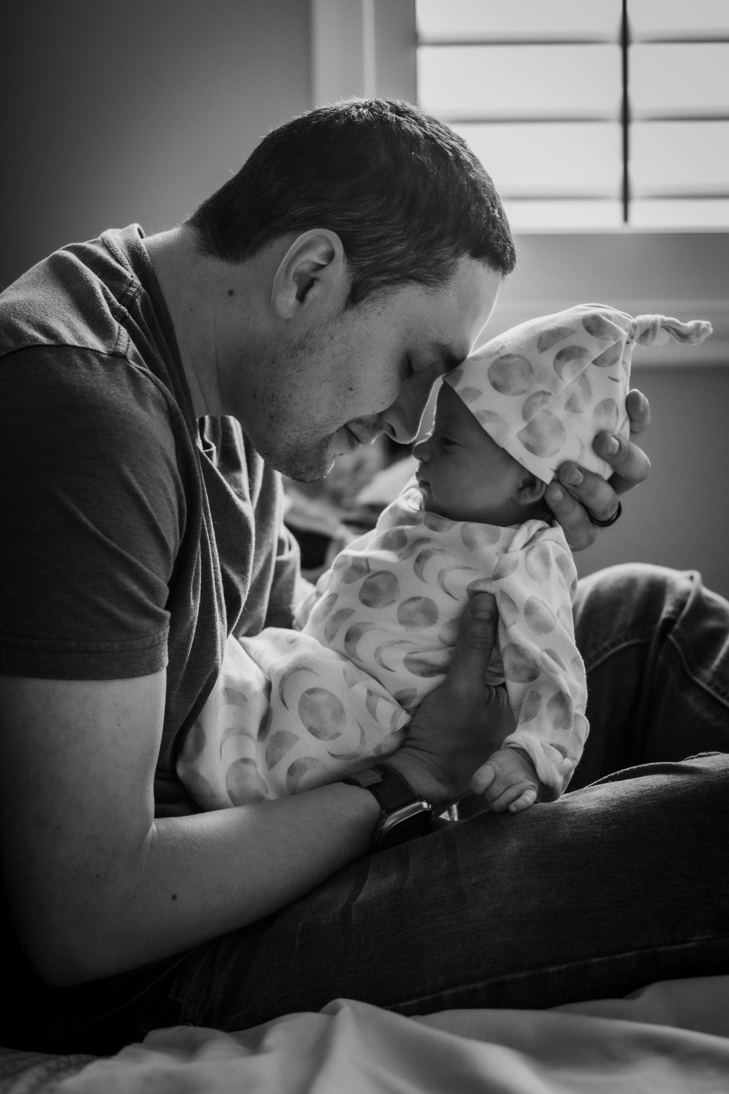 Black and white photo series showing an intimate moment and connection between parent and infant on white bedding.
