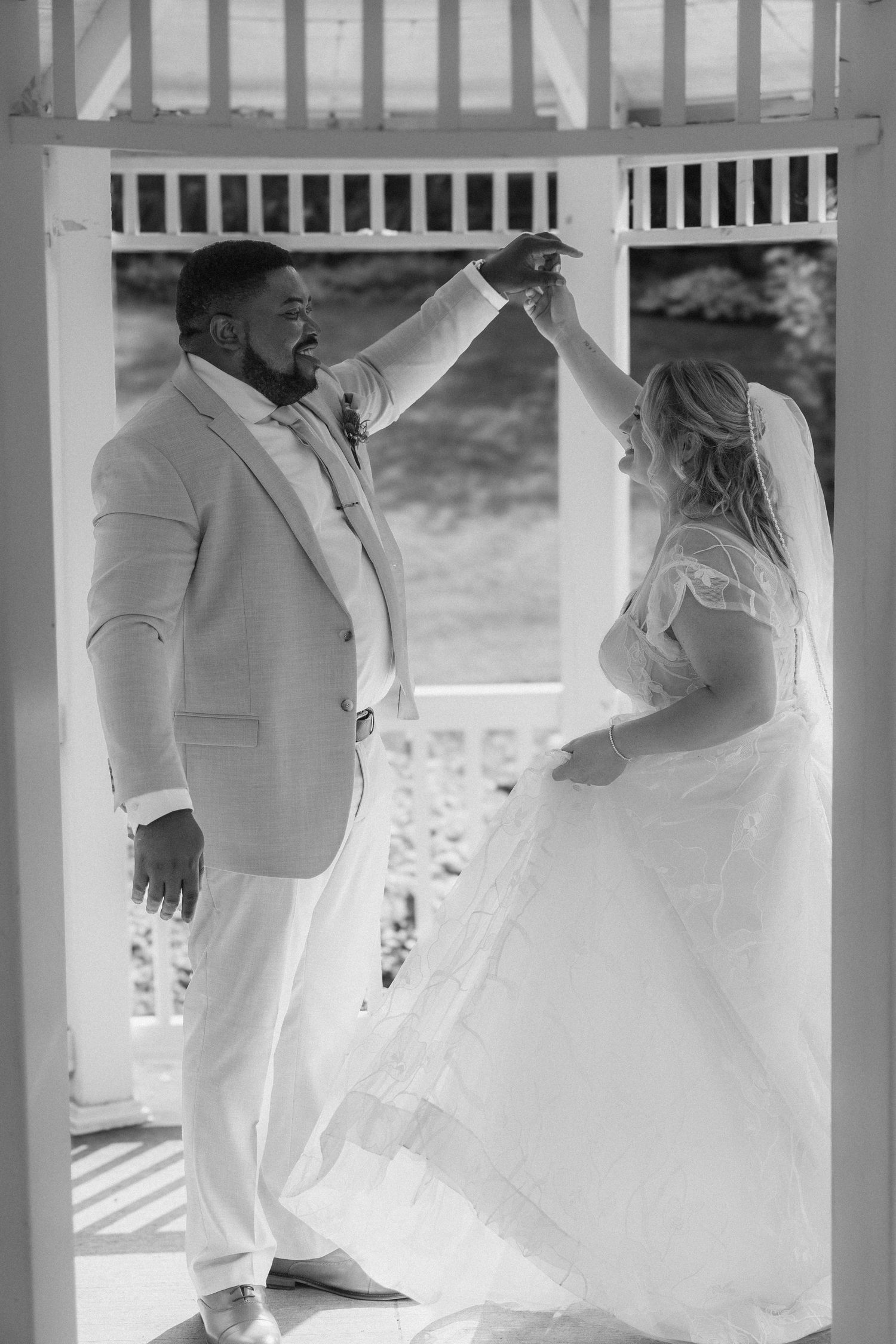 Black and white photo of a bride and groom sharing a first dance in a white gazebo on their wedding day.