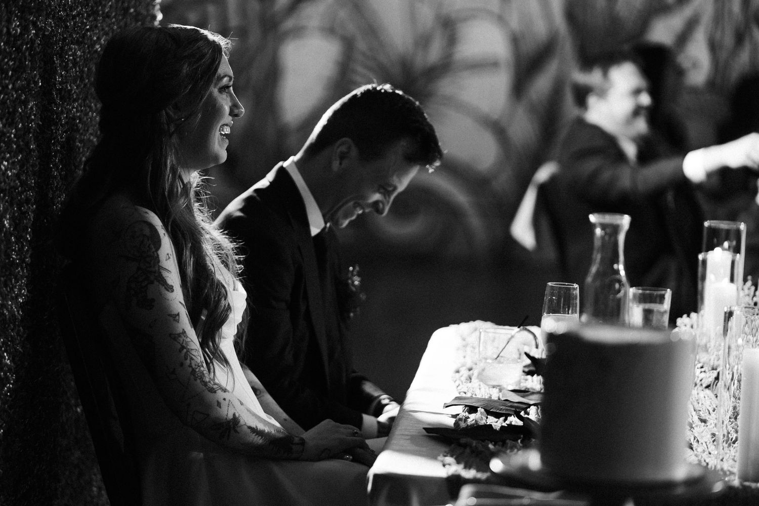 Black and white photo of a bride and groom signing wedding documents at a candlelit table during their ceremony.
