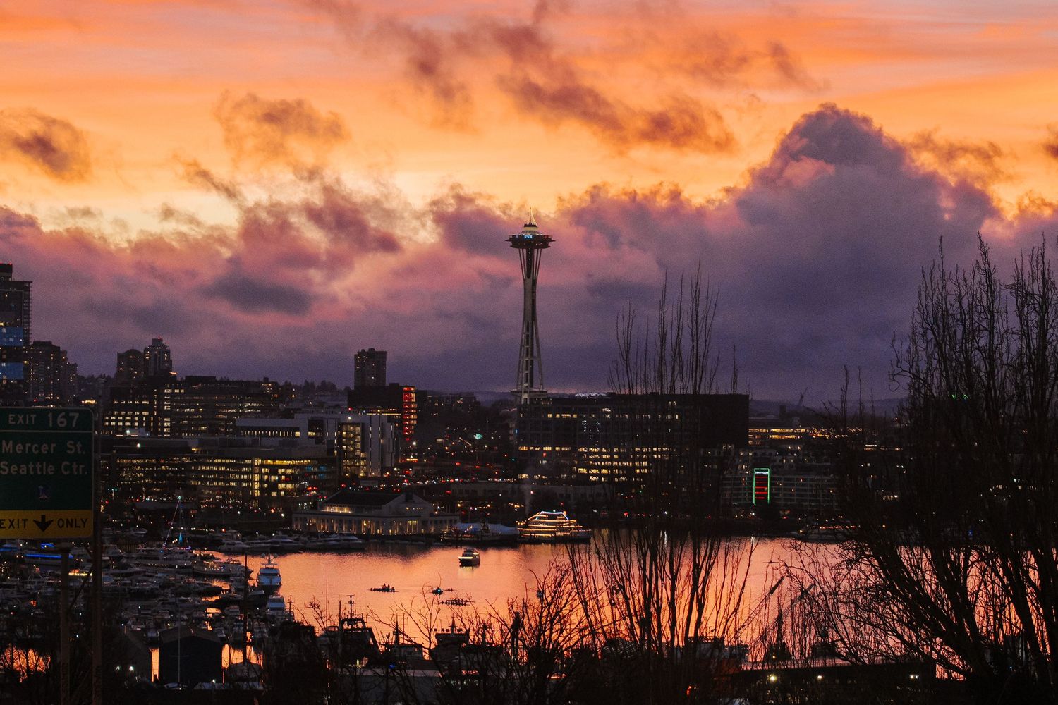 Seattle skyline with Space Needle at dramatic sunset, vibrant orange and purple clouds reflecting on Elliott Bay.