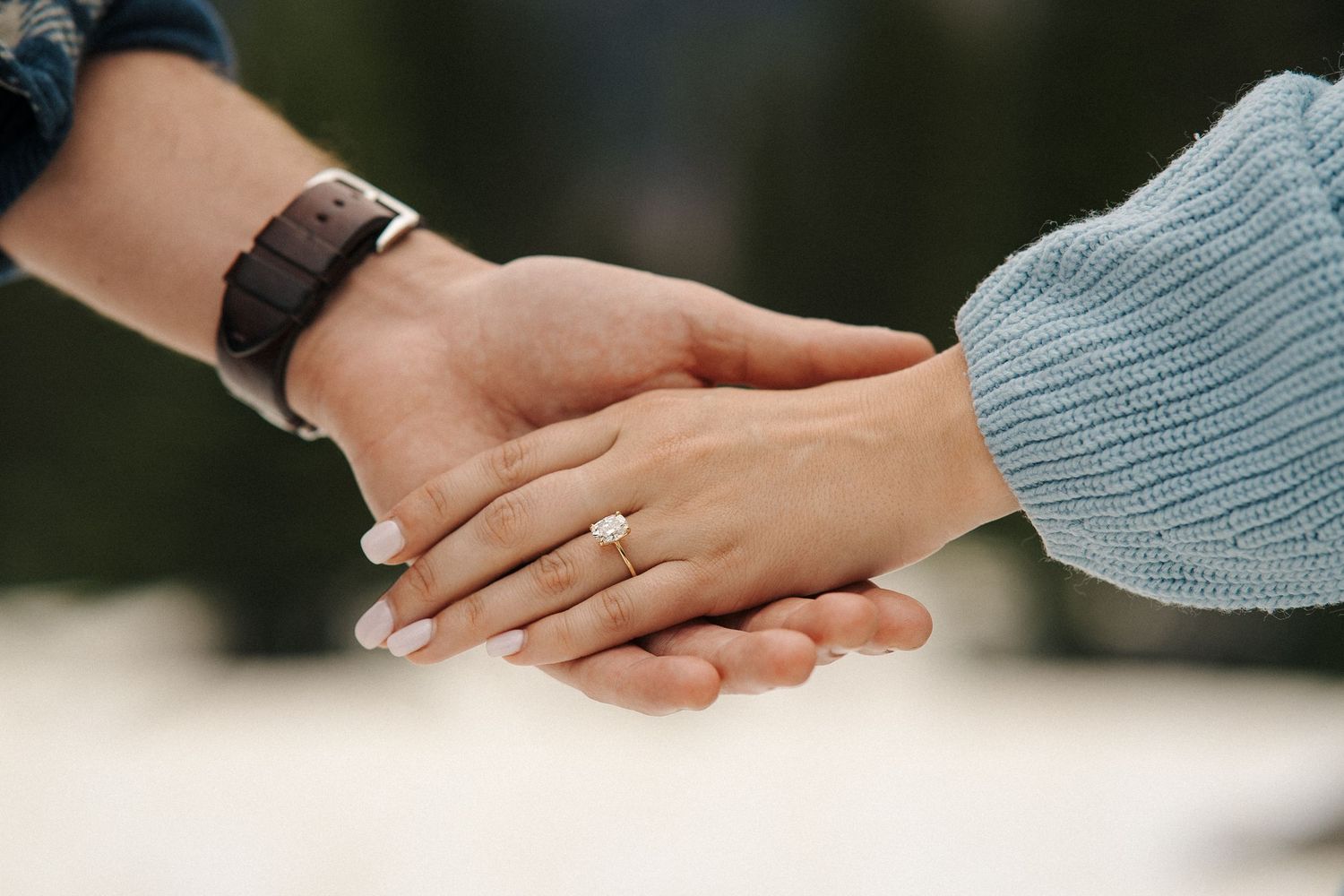 Two hands touching gently with engagement ring visible against soft knitted sweater background.