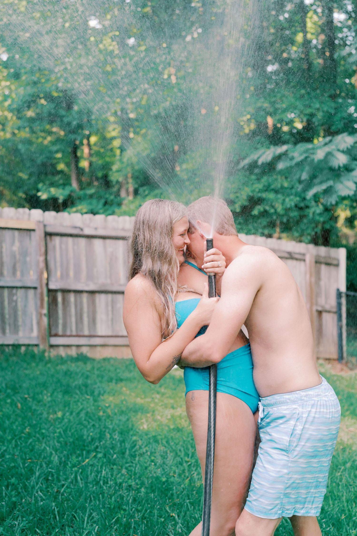 Playful couple spraying each other with a garden hose in a backyard.