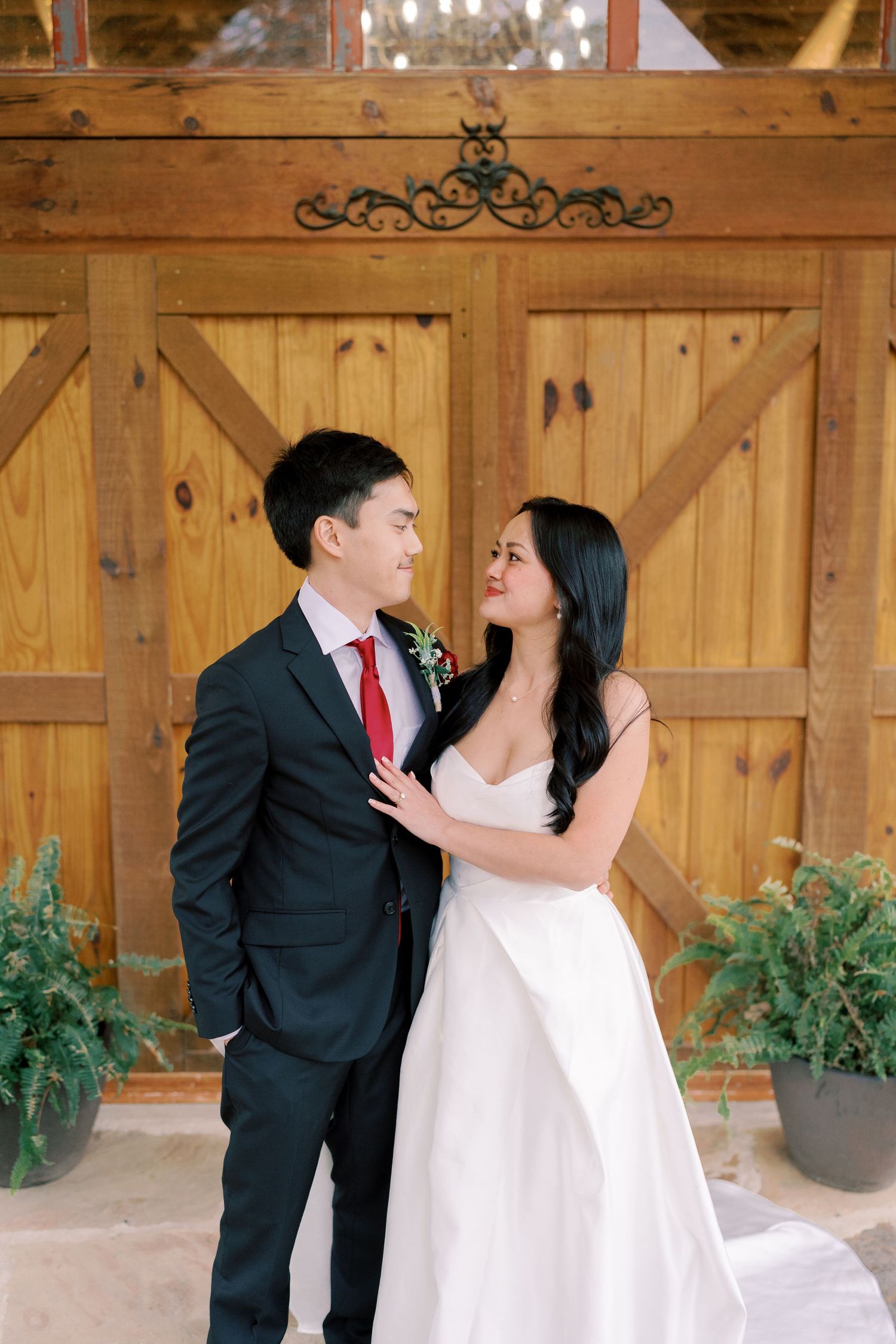 Romantic wedding portraits against rustic wooden barn doors with greenery accents.