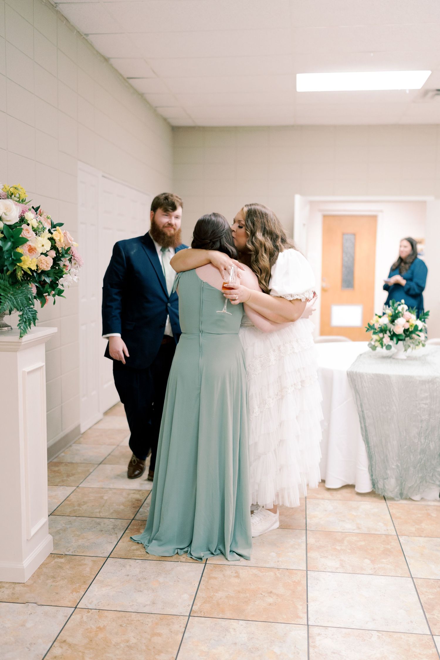 Wedding party sharing an intimate moment in a church hallway with floral decorations.