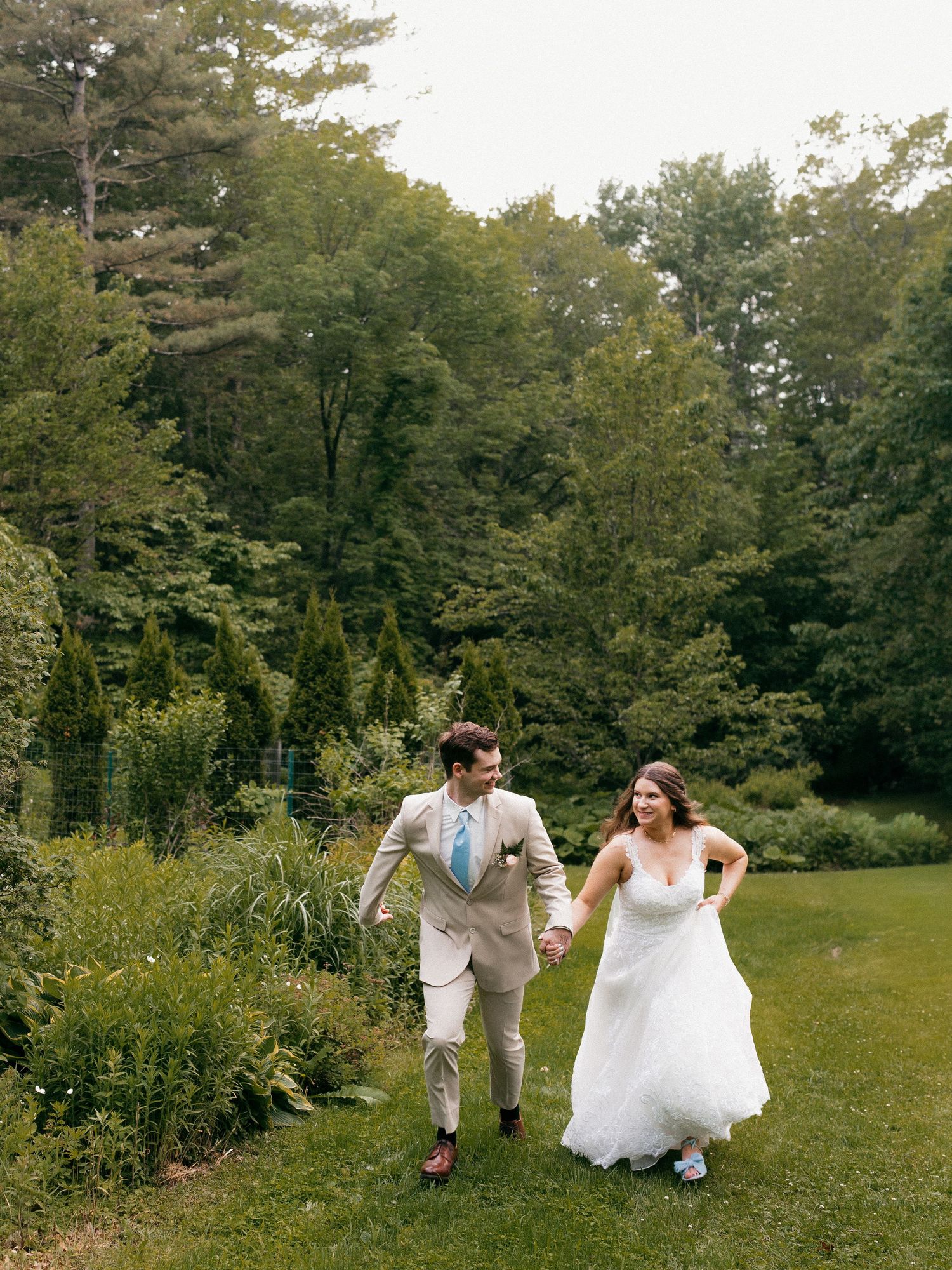 Wedding couple laughing while running through a scenic garden landscape.
