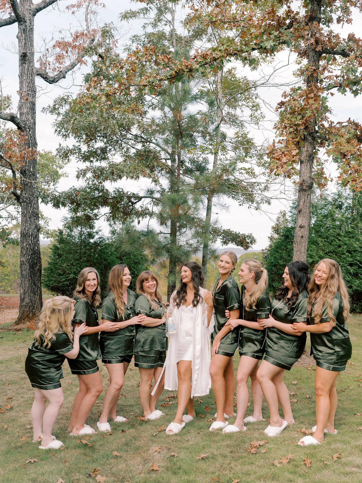 Bridal party in matching olive green outfits poses playfully outdoors.