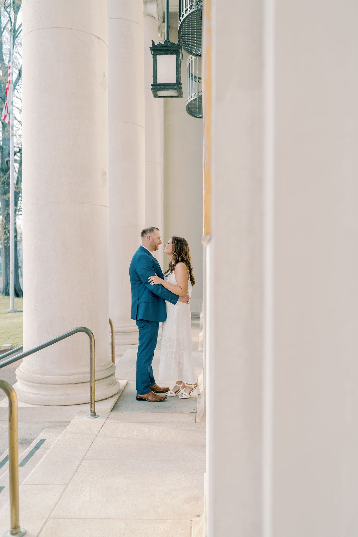 Couple embraces between elegant white columns on classic building porch.