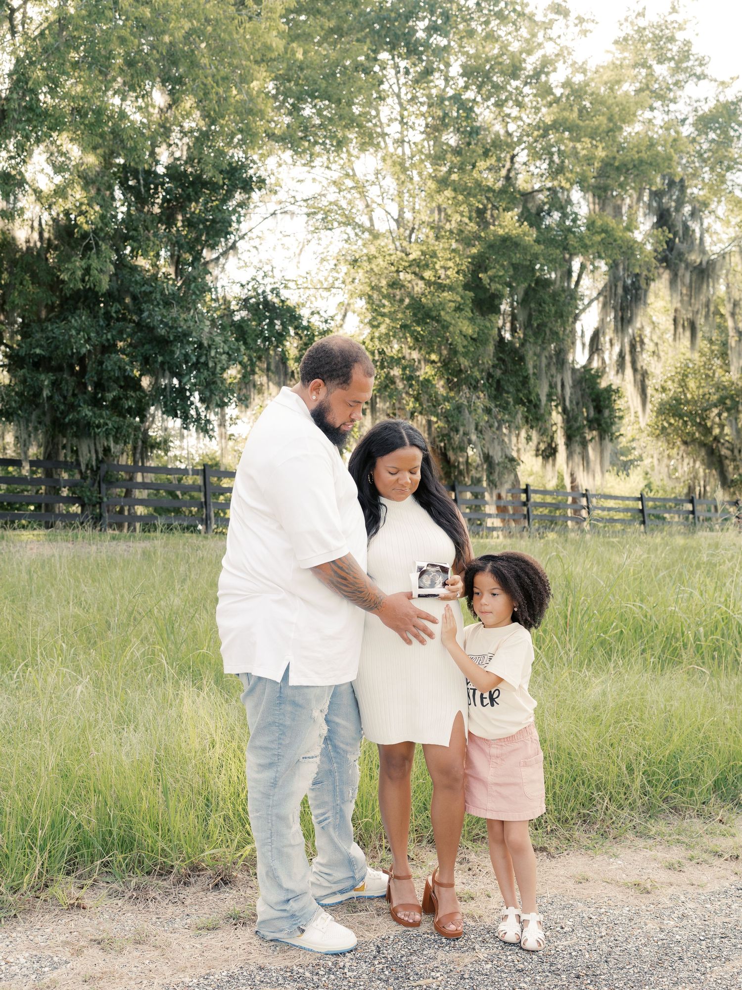 A family shares a tender moment while holding ultrasound photos in a grassy field.