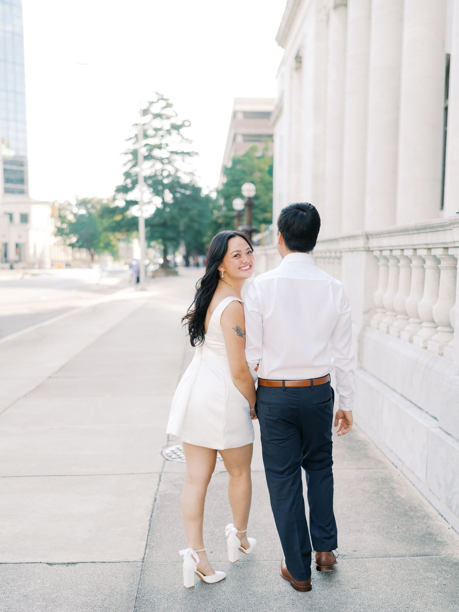 A couple walks hand in hand along a columned walkway wearing coordinated white and navy outfits.