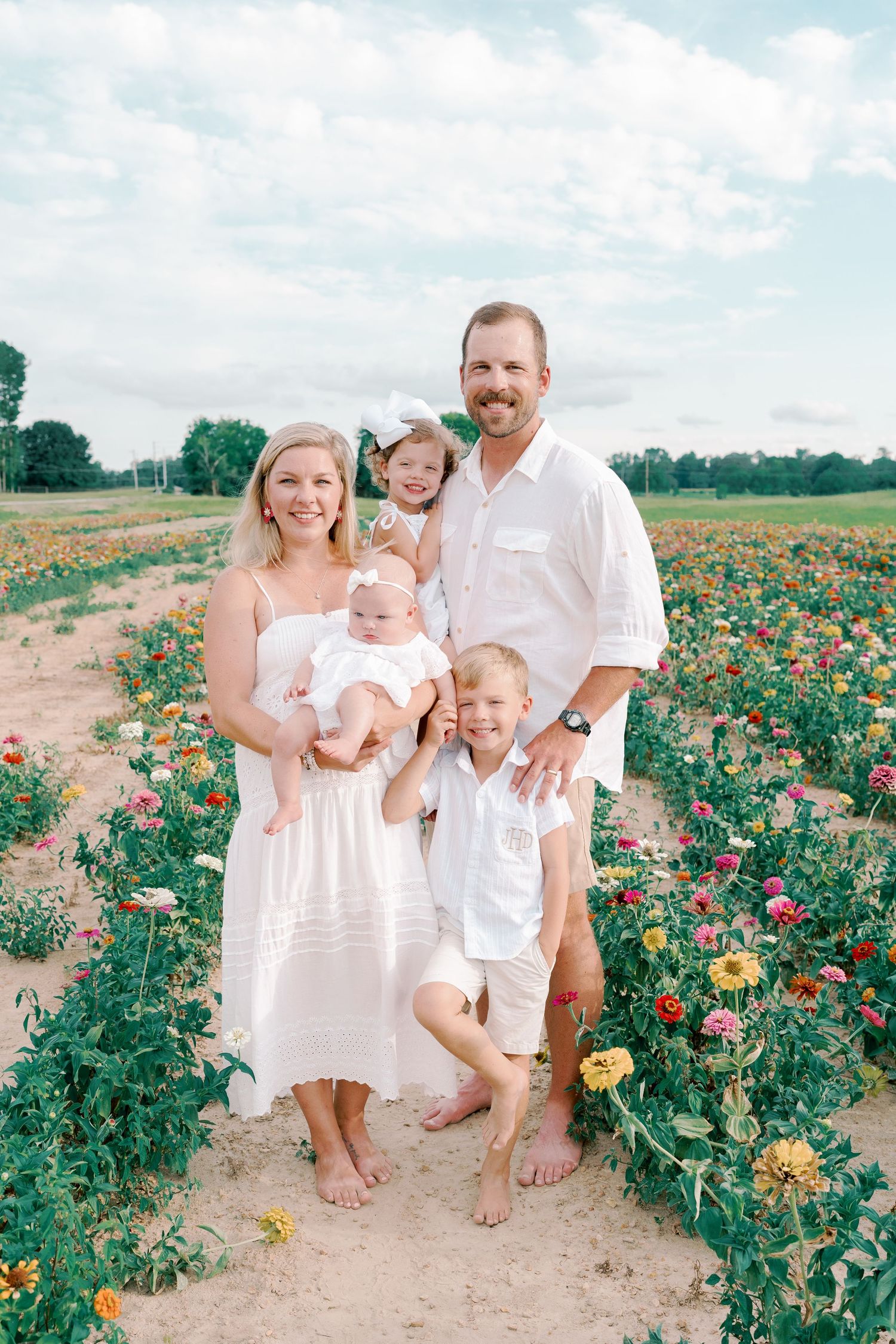 A family gathering poses for photos in a blooming flower field on a sunny afternoon.