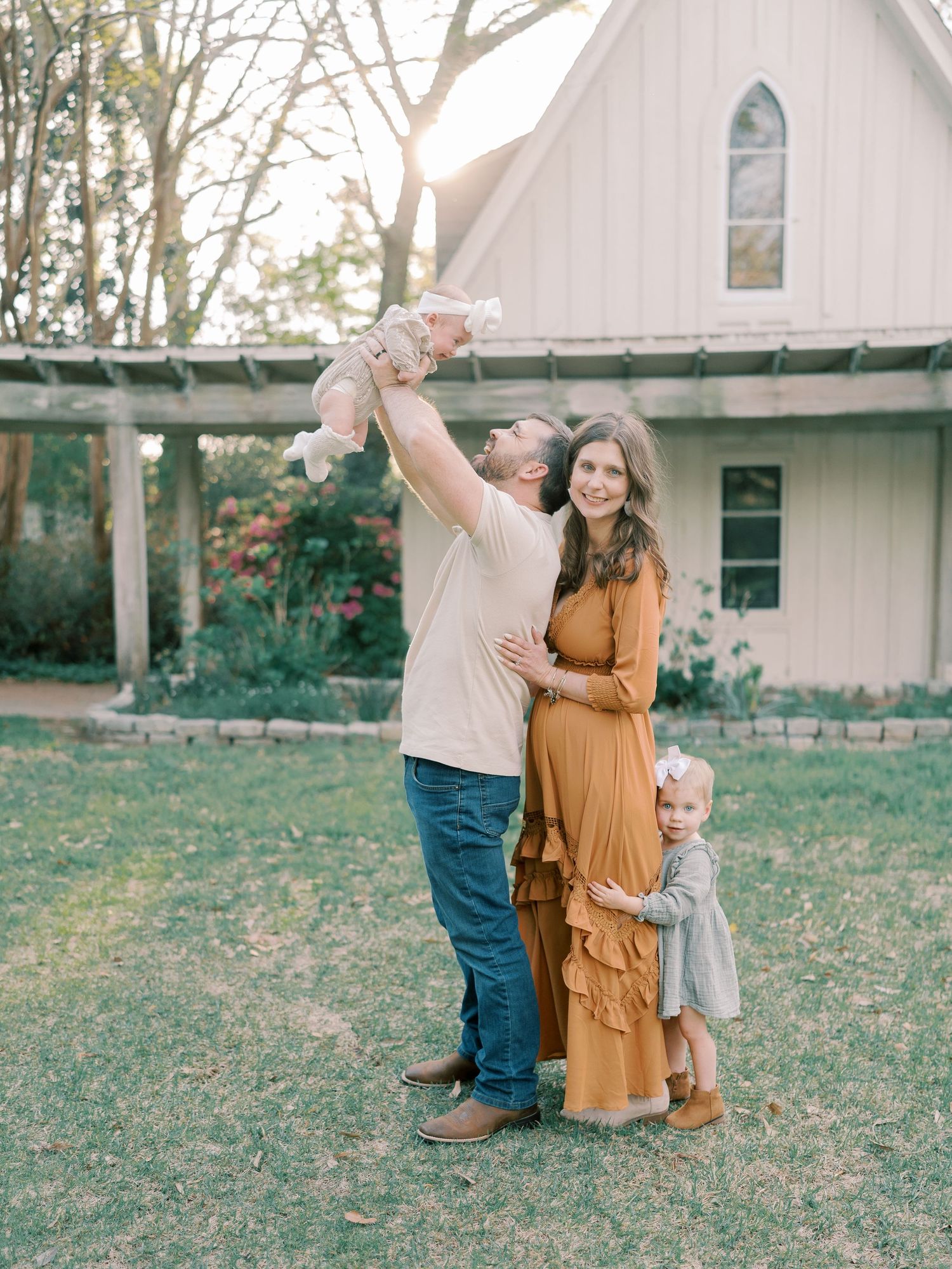 Family plays together on a grassy lawn with a white chapel building in the background.