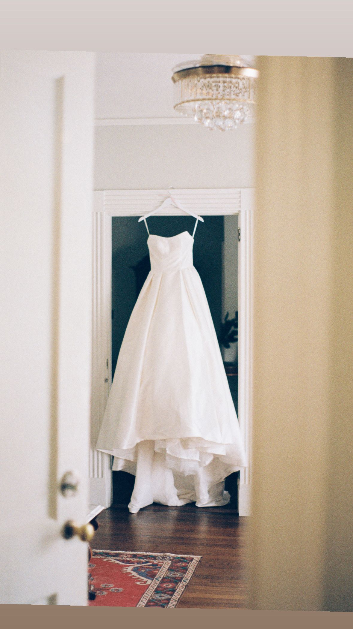 White wedding dress hanging elegantly against a doorway in natural light.