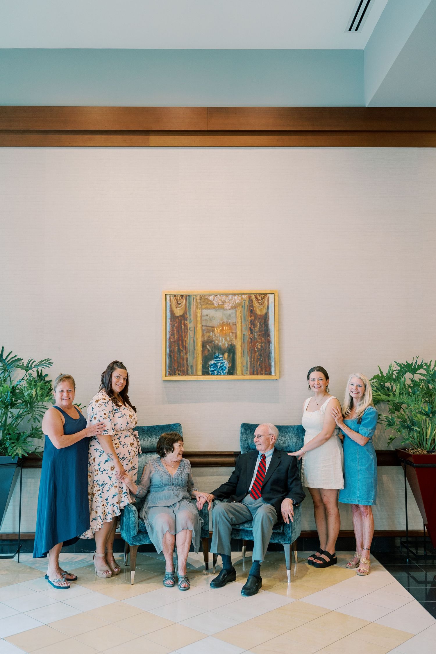 Family group photo with members seated on chairs against white wall with artwork.