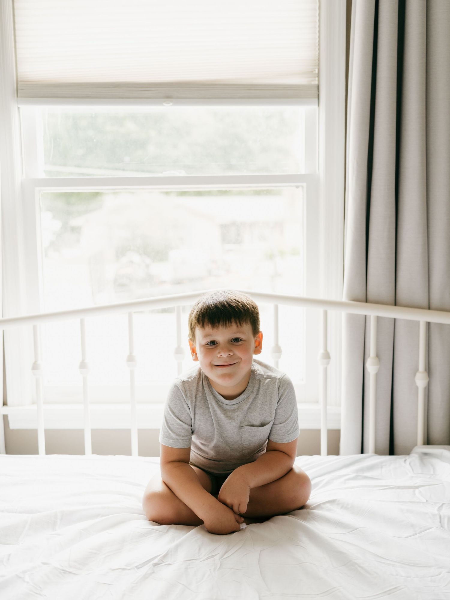 Child lying on white bed near window with soft natural lighting.