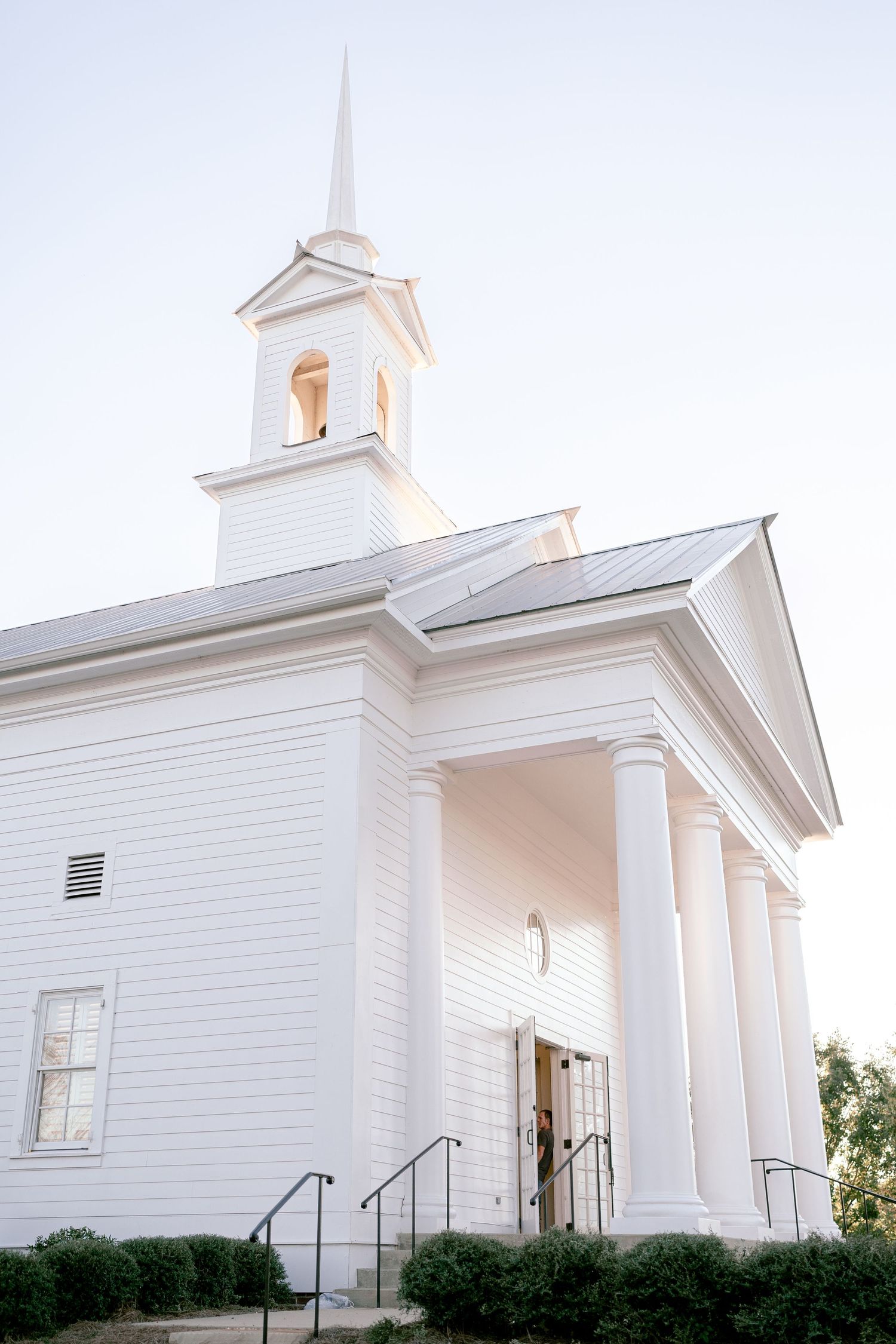 Classic white church with steeple photographed against a bright sky.