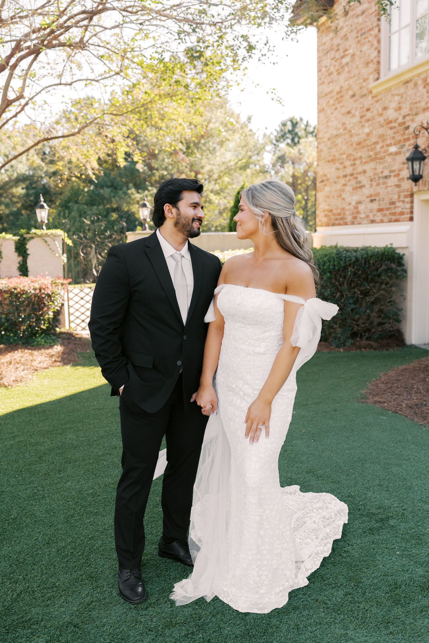 Bride and groom share playful moments on a manicured lawn in front of a brick building.