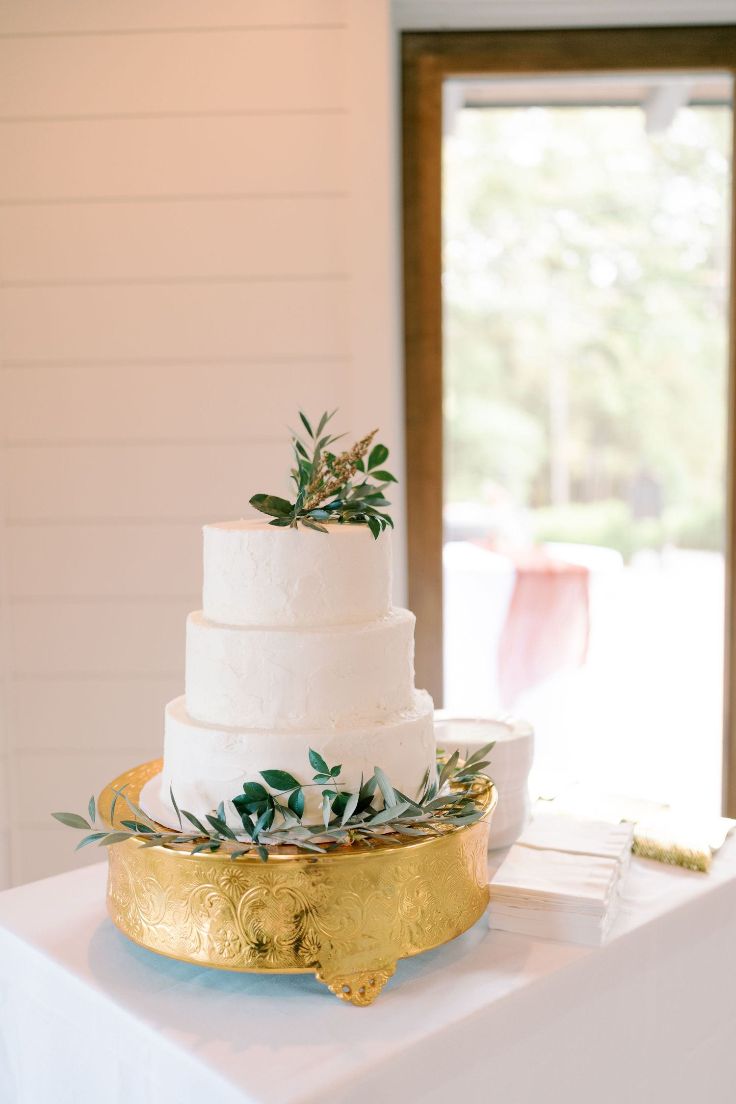 Elegant white wedding cake with gold accents and greenery on display.