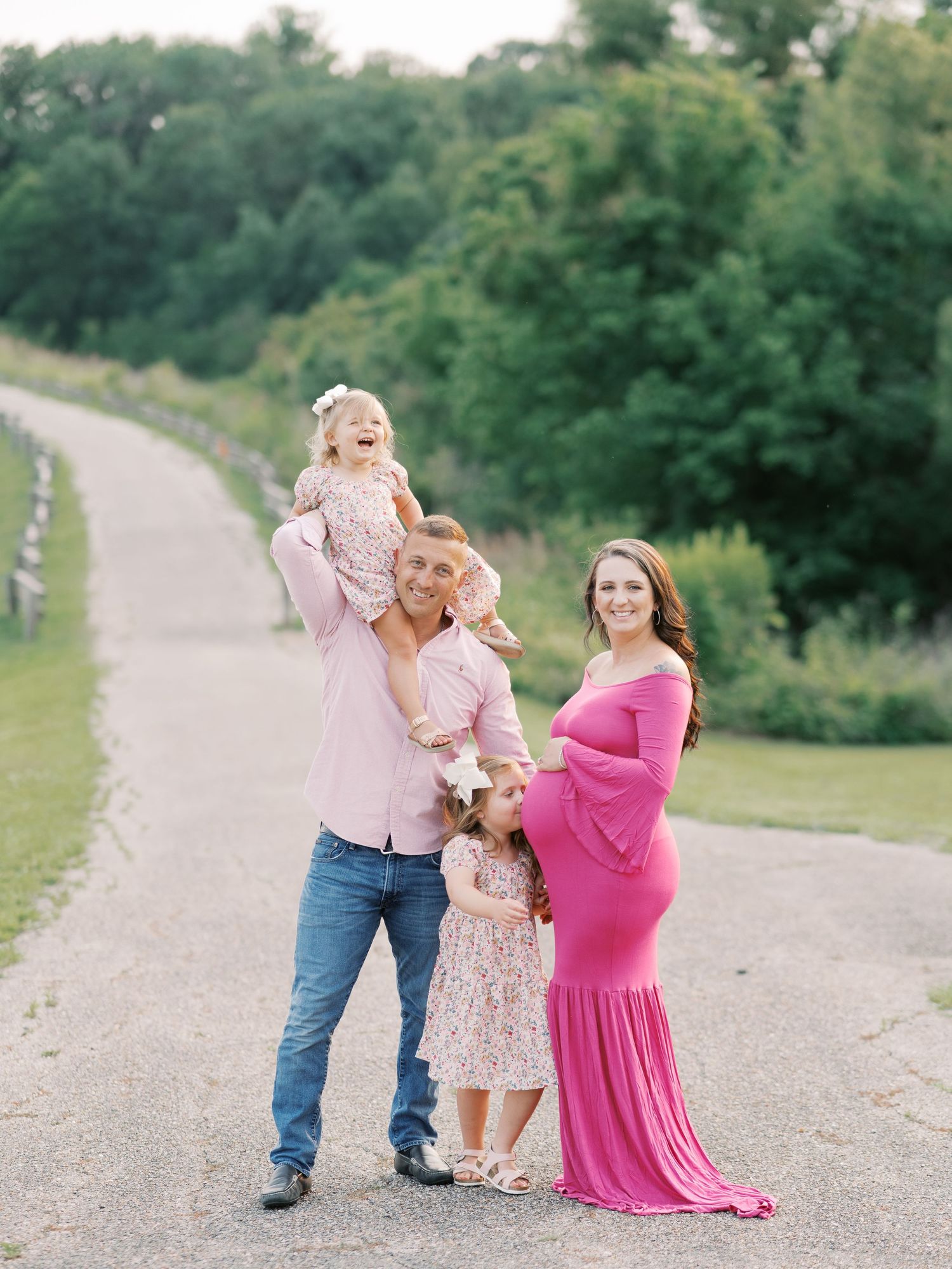Family photo session on a gravel path with parents and child in coordinated pink outfits.