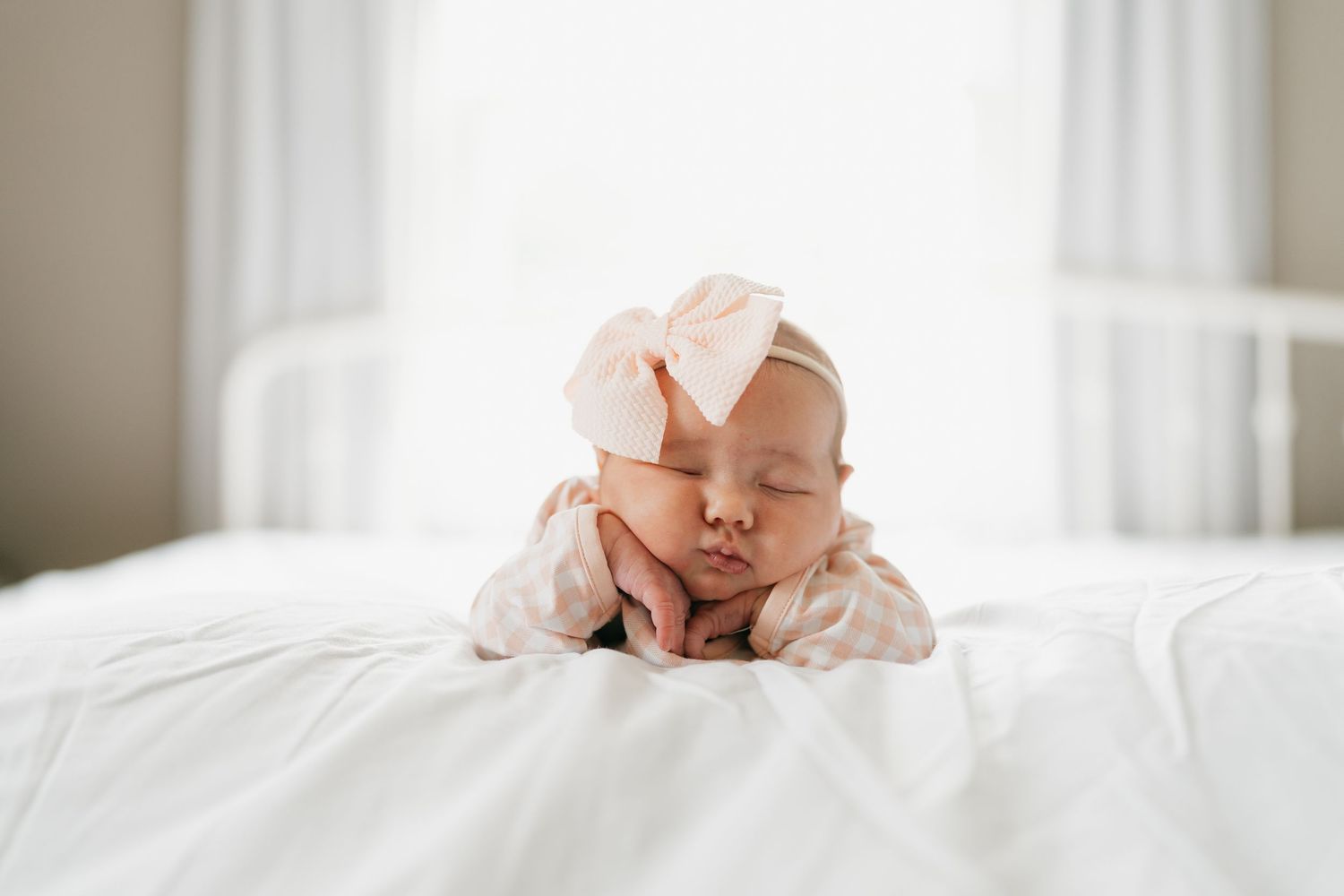 Baby in pink outfit lying on white bedding with eyes closed.