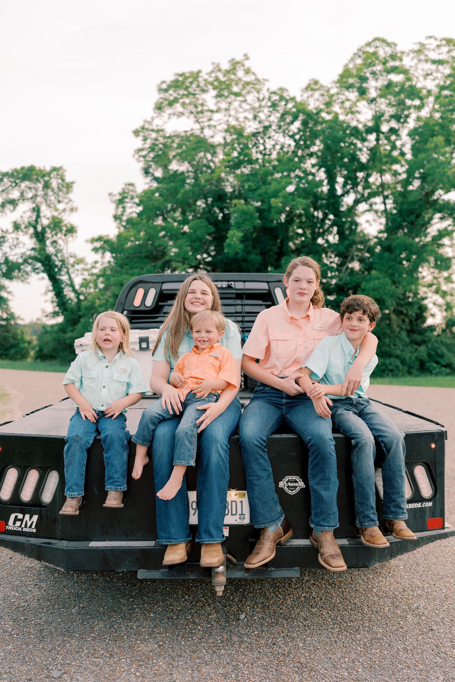 Family members sitting together on the back of a black pickup truck in a casual outdoor setting.